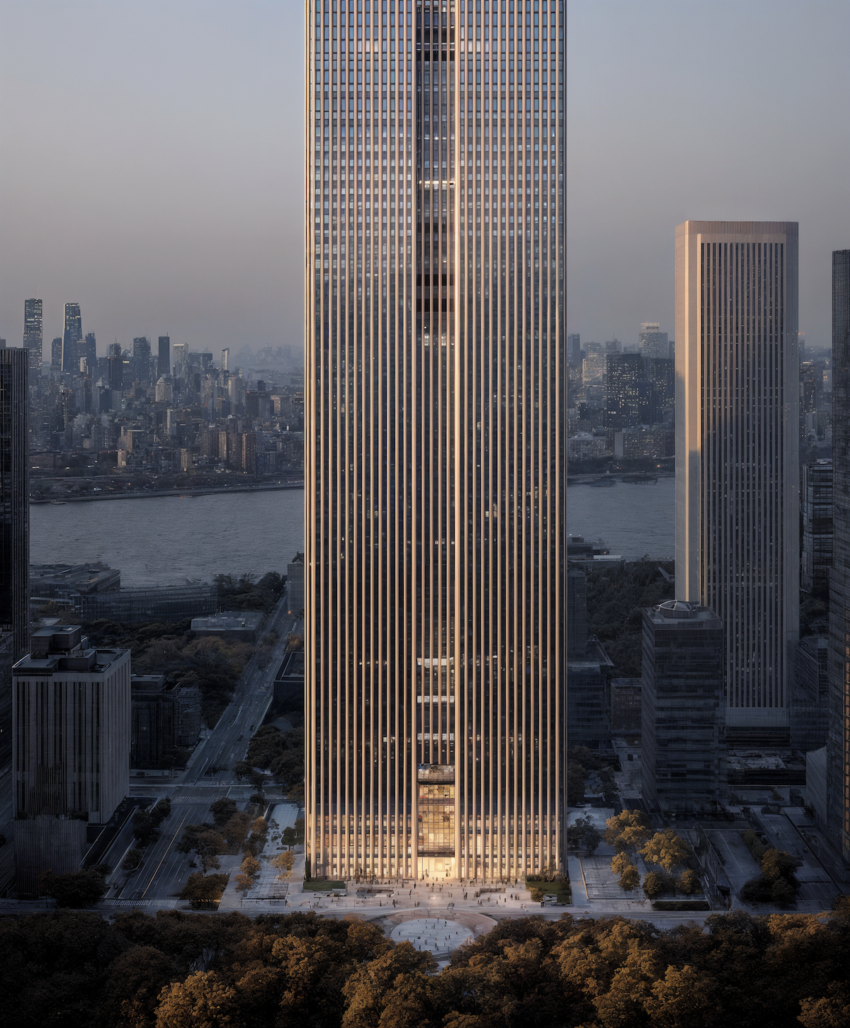 Tall modern skyscraper with vertical lines illuminated by evening light, situated in a cityscape with a river and other high-rise buildings in the background.