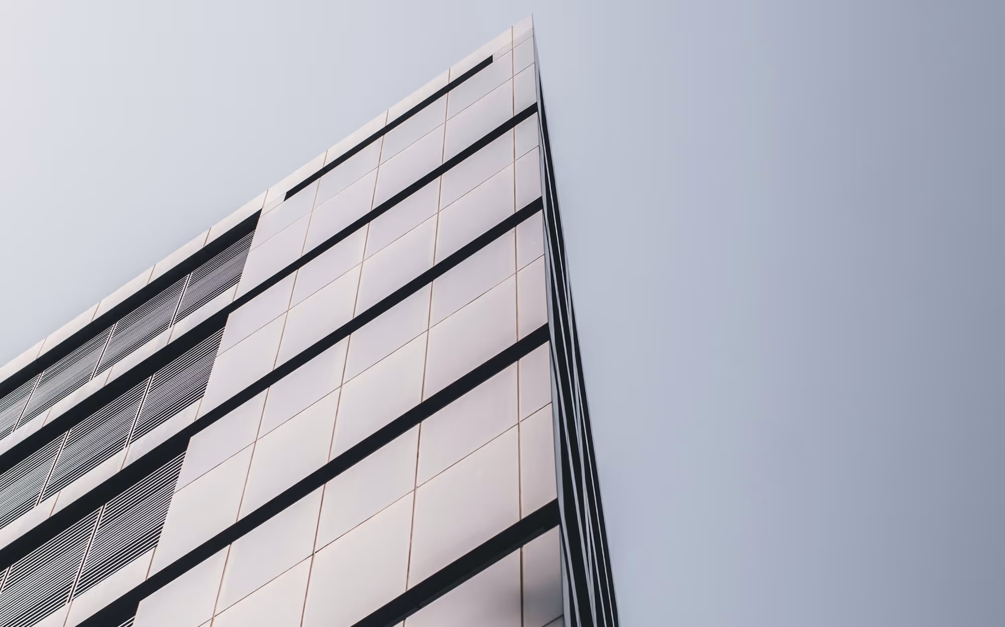 Upward angled view of a modern building with reflective glass panels and black horizontal dividers against a clear sky.