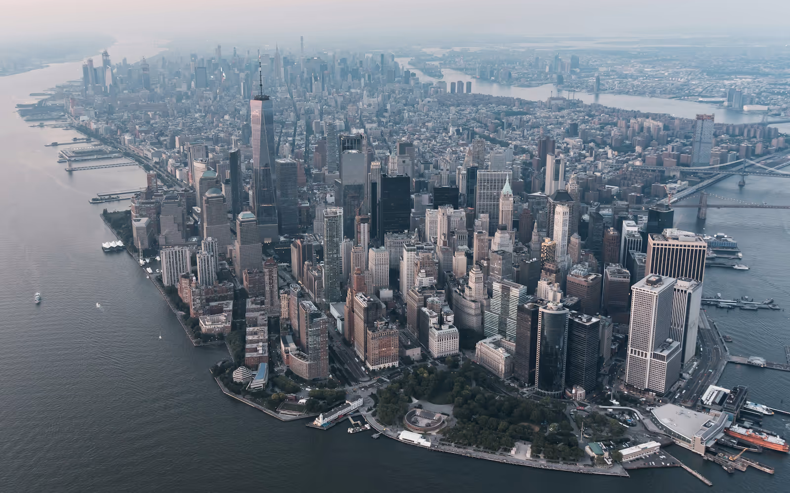 Aerial view of Lower Manhattan in New York City, showing skyscrapers, waterfront, and bridges in the distance.