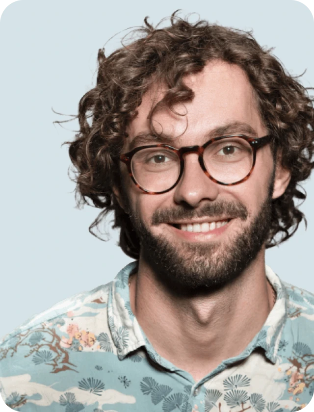 A man with curly hair and glasses smiling.