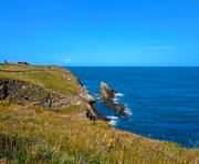 Cliffside with green grass overlooking blue ocean under a clear sky.