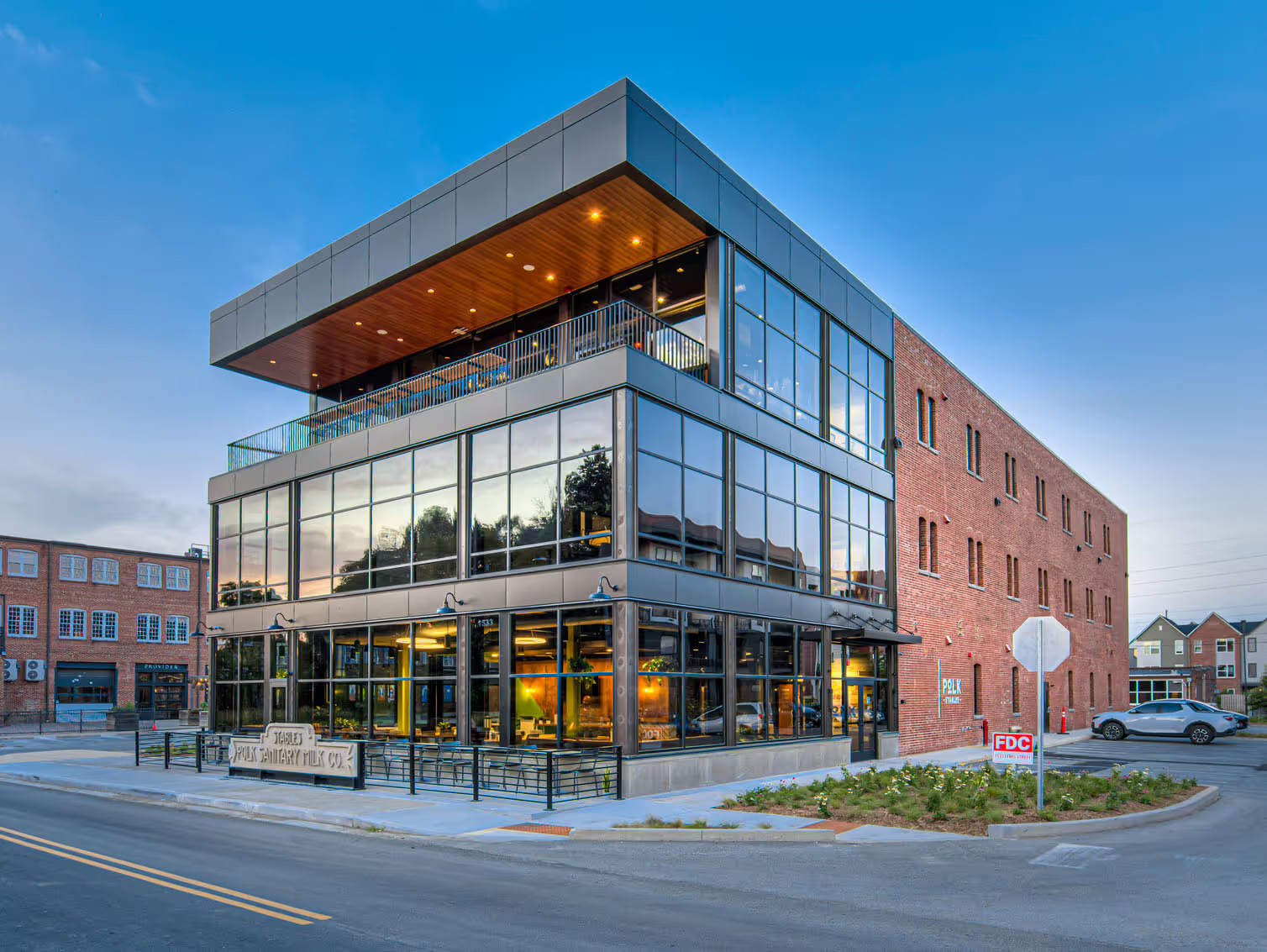 Modern two-story building with large glass windows and a brick facade at dusk on a street corner.