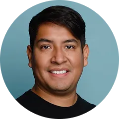Man with short dark hair smiling against a blue background.