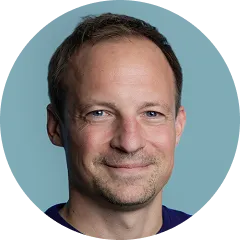 Portrait of a smiling man with short brown hair and blue eyes against a blue background.