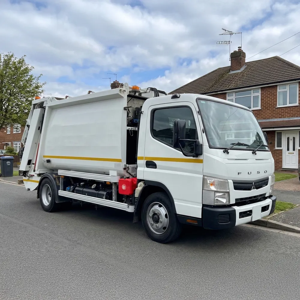 White Fuso refuse collection truck with yellow stripe parked outside a large industrial building.