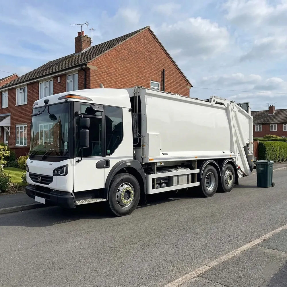 White DAF LF refuse collection truck parked on wet concrete in front of a blue industrial building.