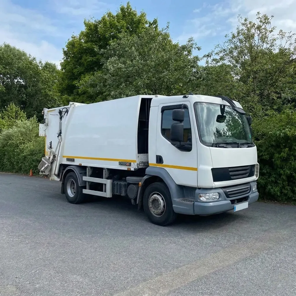 White Fuso refuse collection truck with yellow stripe parked outside a warehouse with gray metal siding.