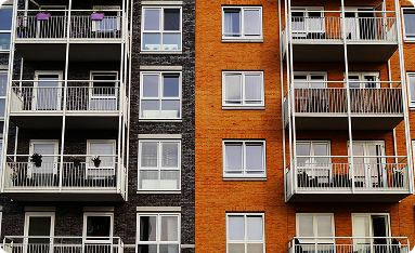 Fassade eines modernen Mehrfamilienhauses mit Balkonen und Fenstern, teils mit schwarzer und teils mit orangefarbener Ziegelwand.