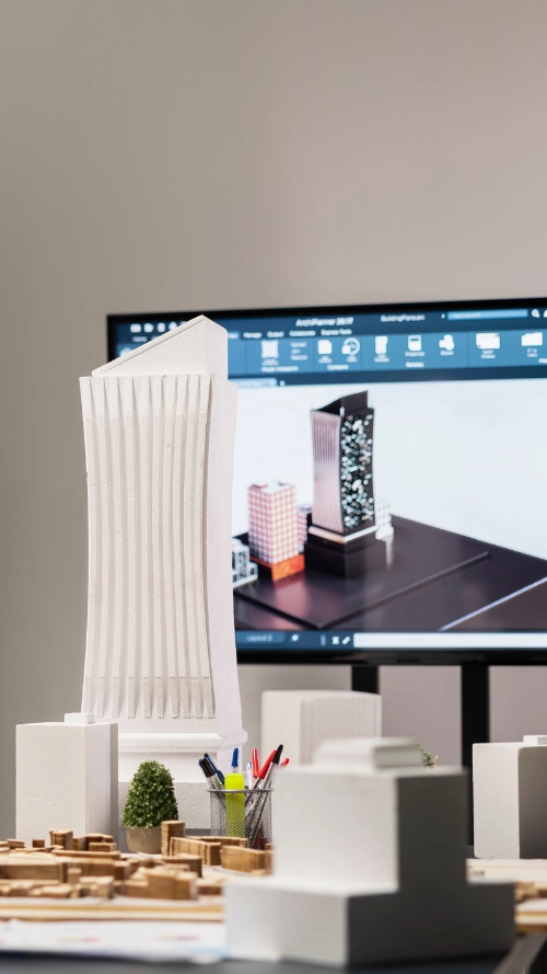 Man using tablet while standing next to architectural white building models in an office with two women working in the background.