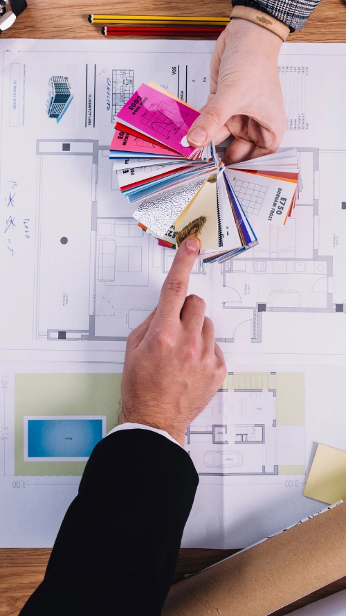 Architectural workspace with color swatches, drafting tools, a tablet displaying a floor plan, and a keyboard on a blue surface.