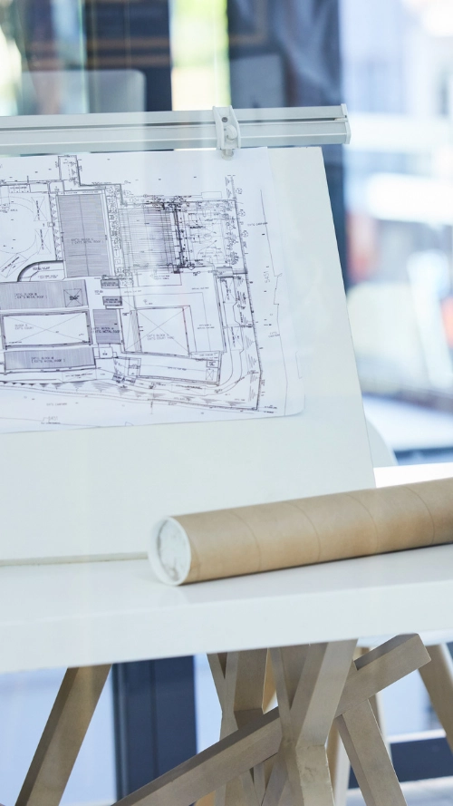 Modern architectural model of a multi-level building with curved glass walls and a circular rooftop feature, placed on blueprints.