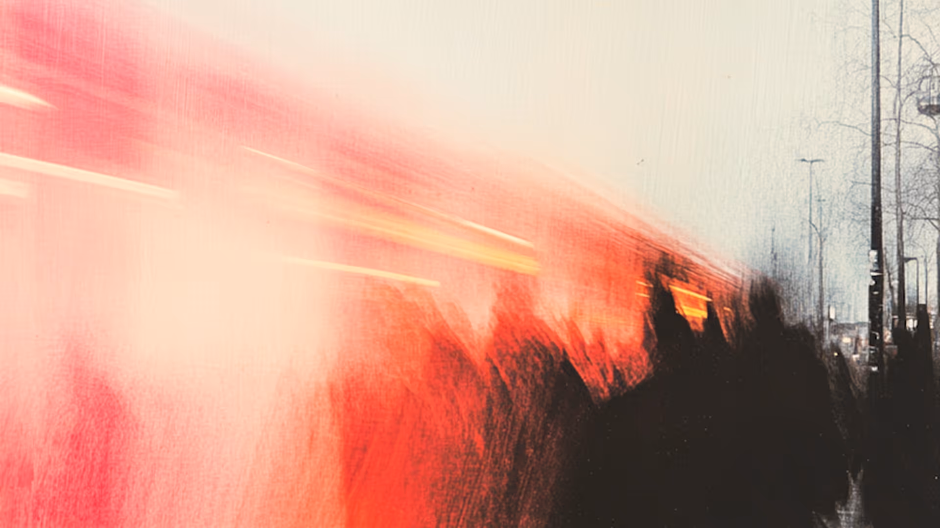 Blurred motion of a red train passing by at a station with silhouettes of waiting people and lampposts.