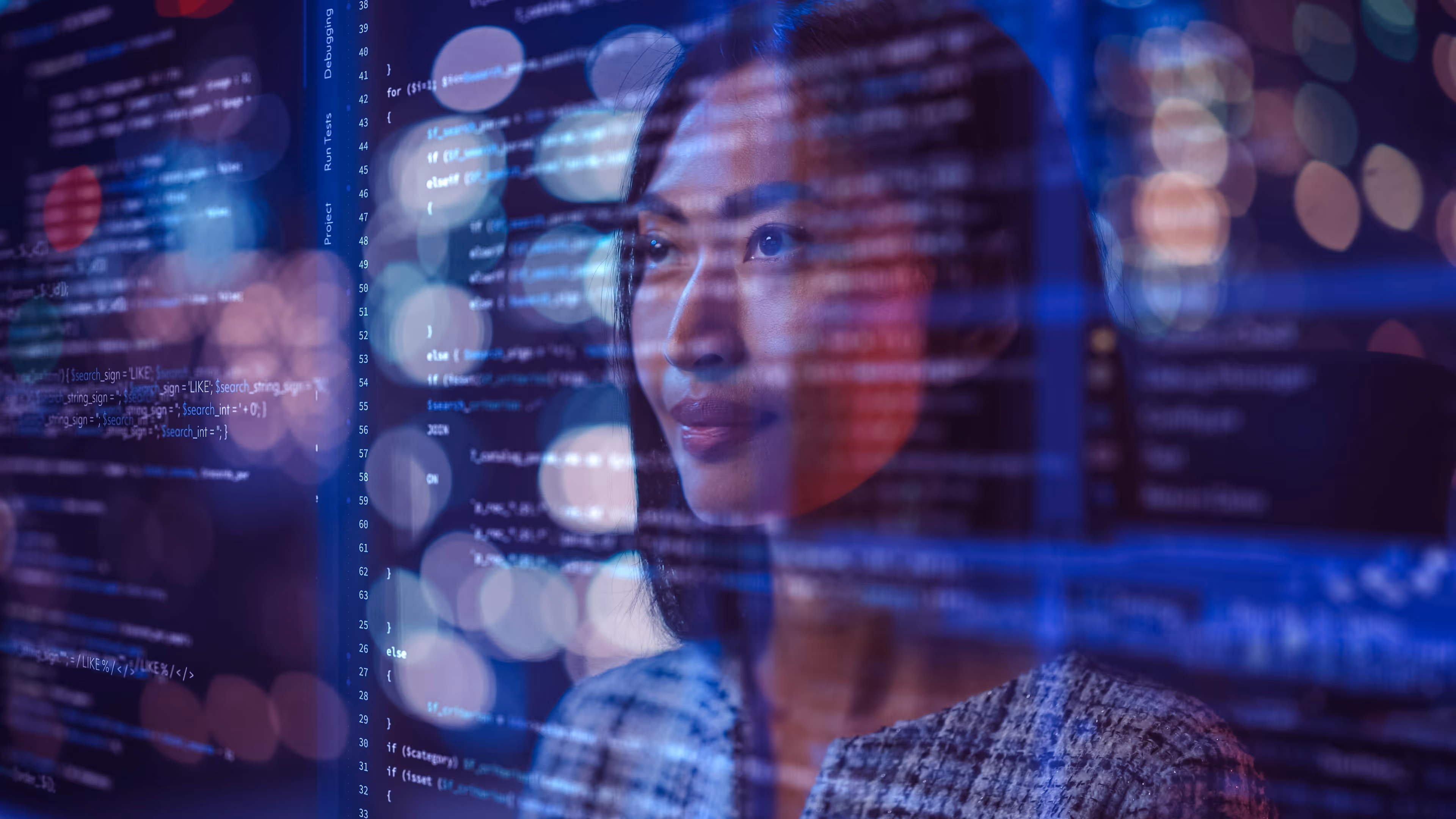 Focused woman looking at transparent screens with computer code and city lights blurred behind.