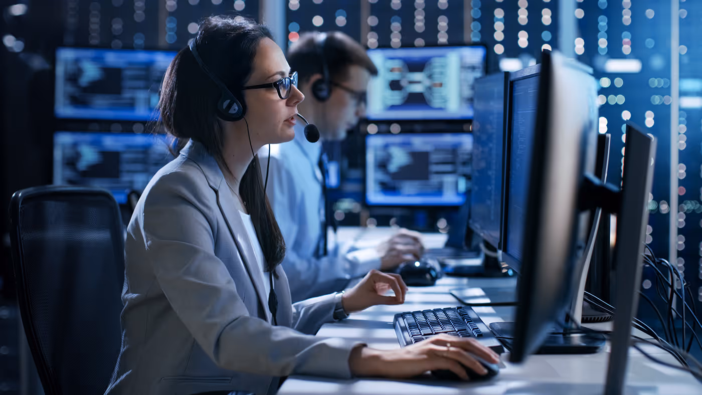 Two customer service agents with headsets working on computers in a tech support call center.