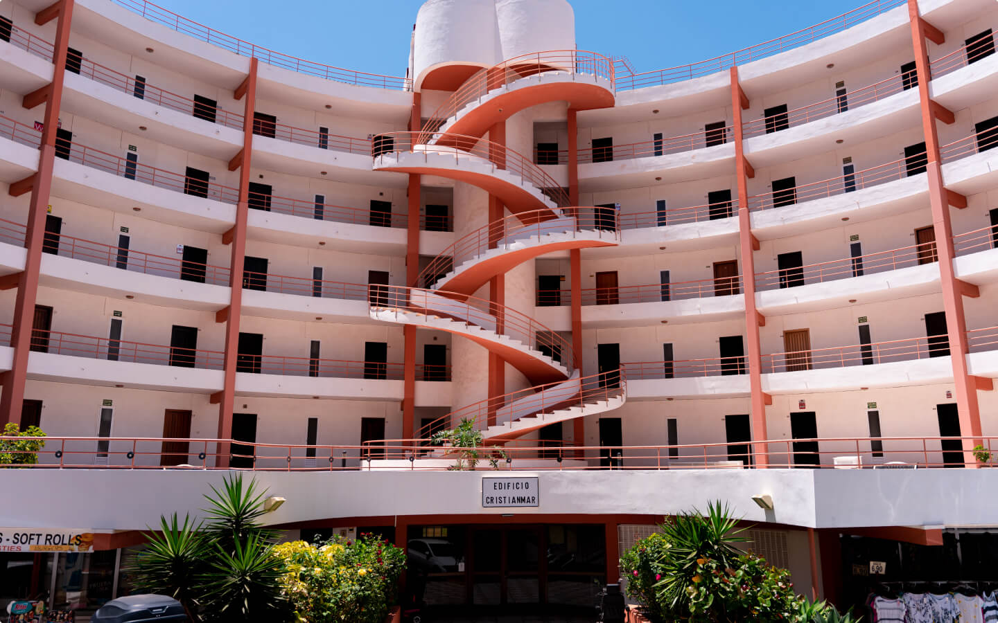 Curved white apartment building with red railings and a central spiral staircase under clear blue sky.