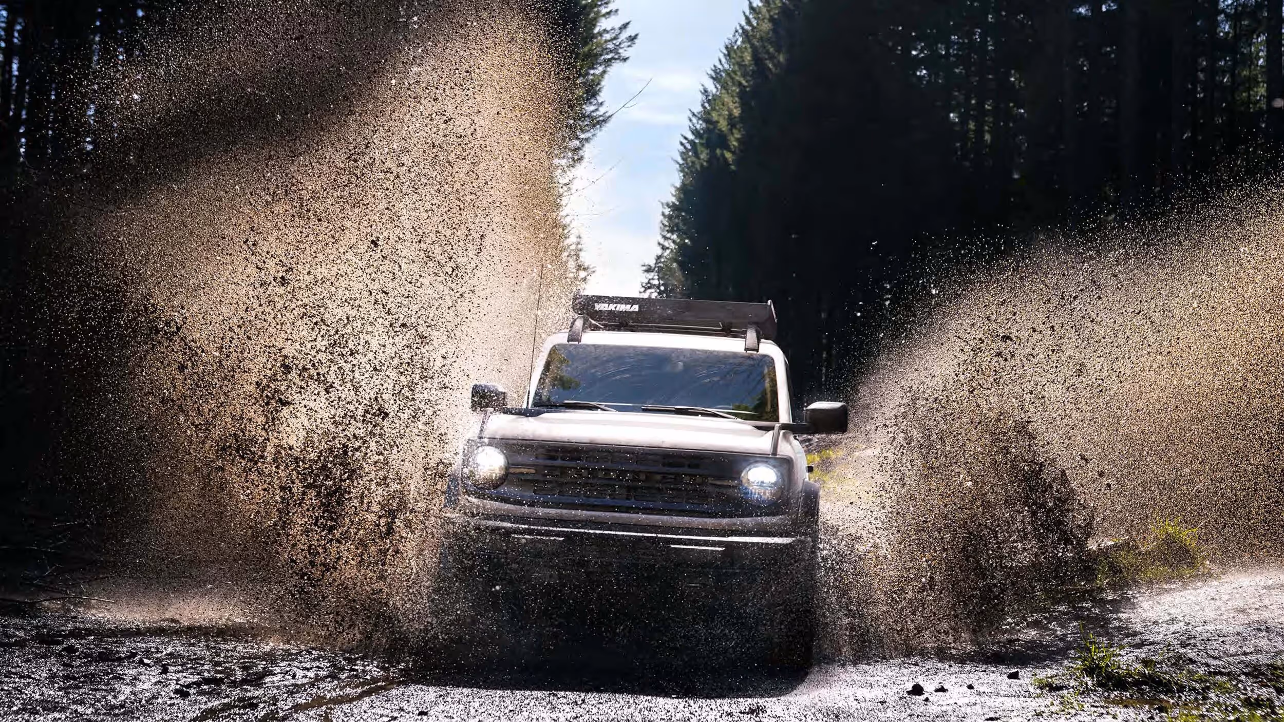 Ford Bronco splashing through mud on a rugged forest trail.