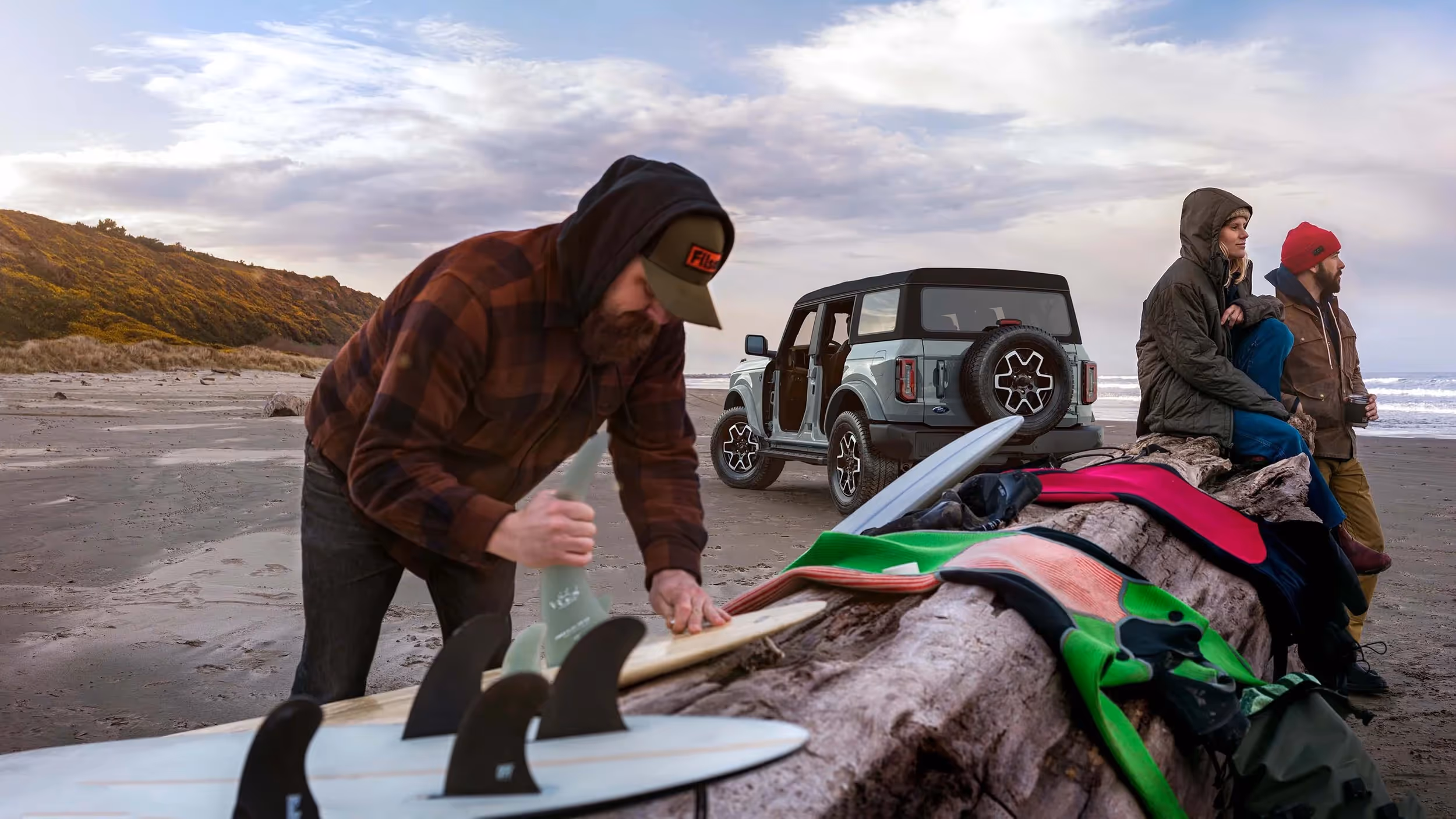 Crew unloading surfboards beside a Ford Bronco at the beach.