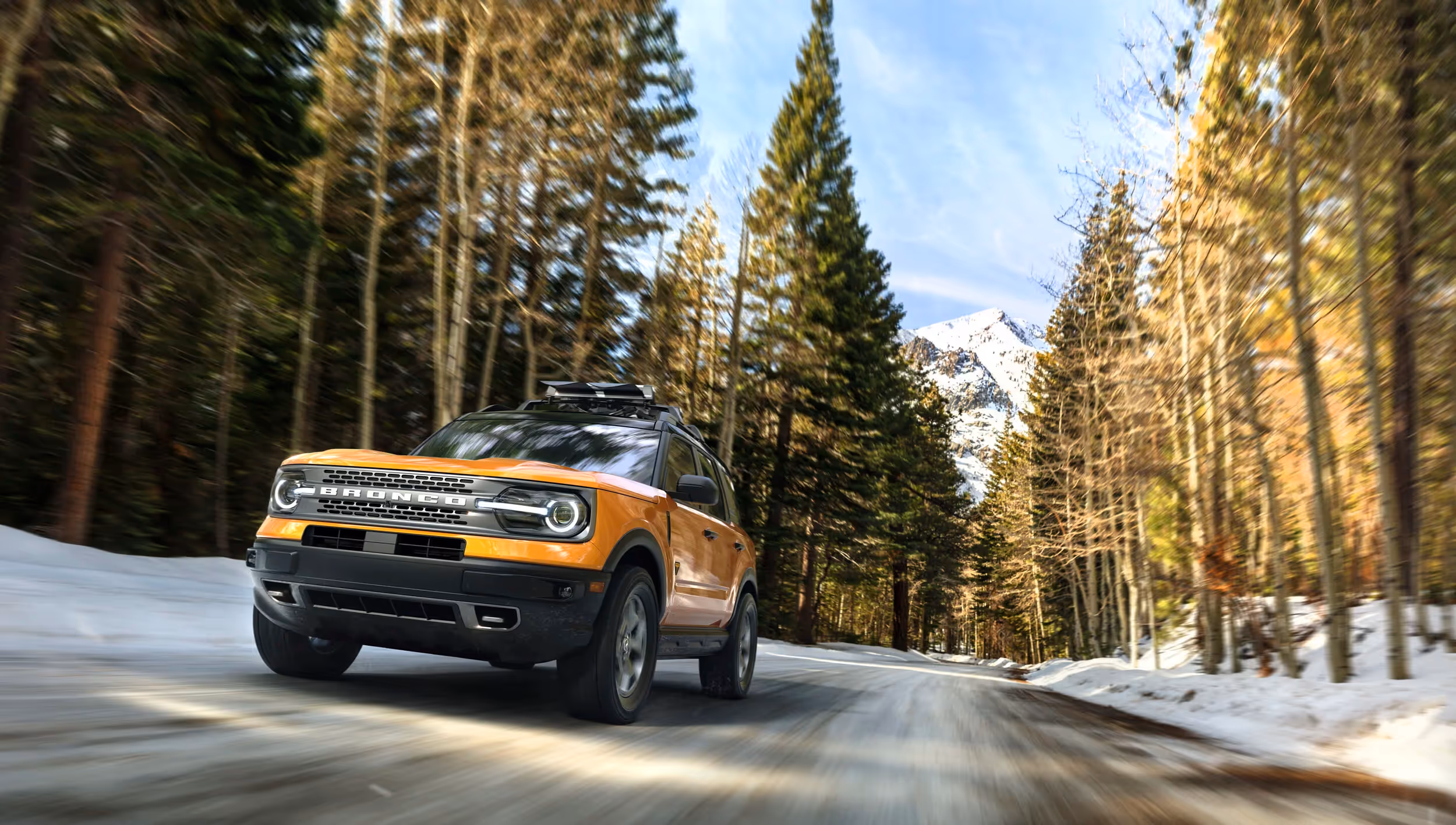 Orange Ford Bronco Sport driving through snowy mountain forest road, dynamic winter adventure automotive photography by Roe Photo.