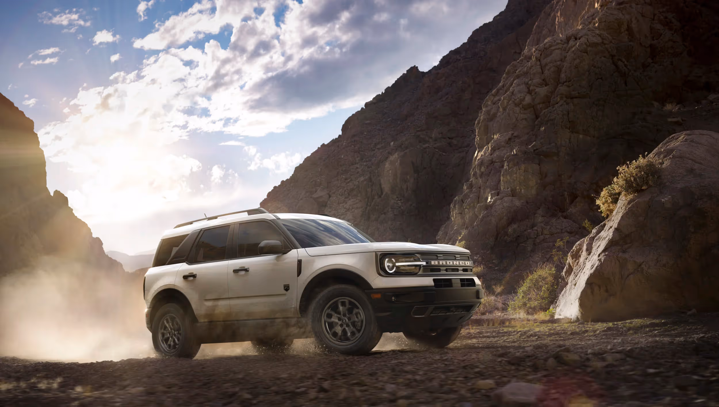 White Ford Bronco Sport kicking up dust in desert canyon at sunset, motion automotive photography by Roe Photo.