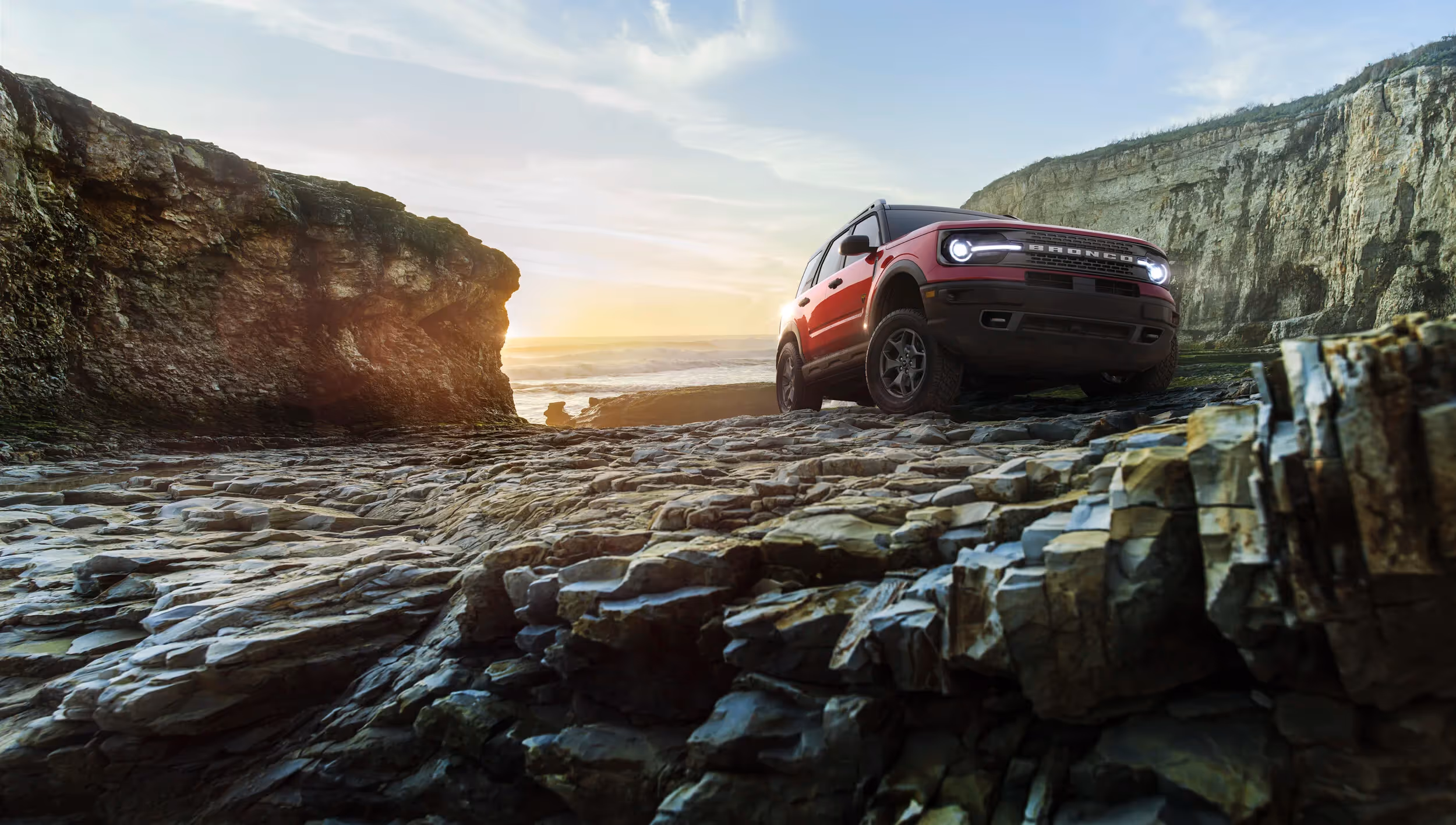Red Ford Bronco Sport navigating rocky coastal terrain at sunset.