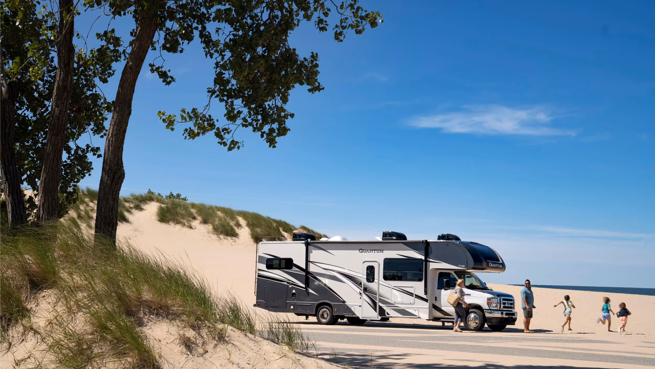 Family arriving at sandy beach in Quantum RV under blue skies, summer travel and outdoor recreation photography by Roe Photo.