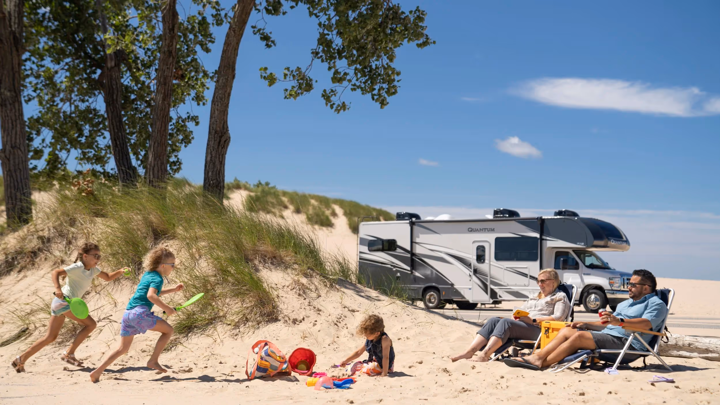 Children playing in sand near Quantum RV parked at lakeshore, family beach camping and adventure lifestyle photography by Roe Photo.