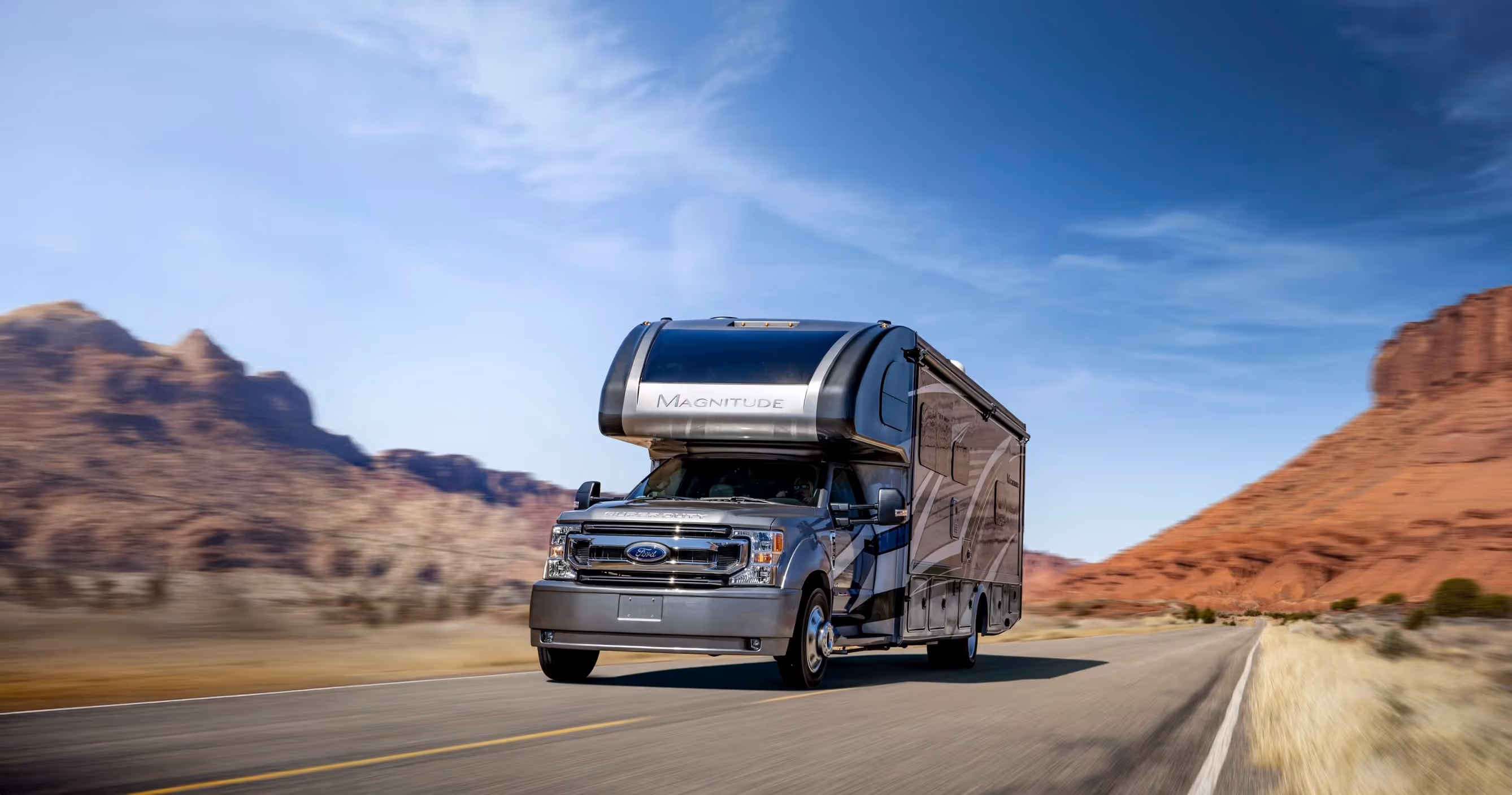 Ford Magnitude Super C motorhome driving on an open desert highway under a clear blue sky.