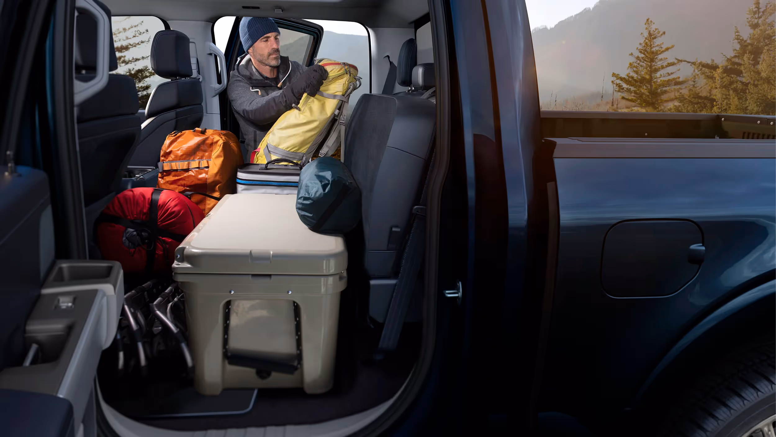 Interior of a Ford F-150 packed with camping gear and a cooler, sunlight filtering through trees outside.