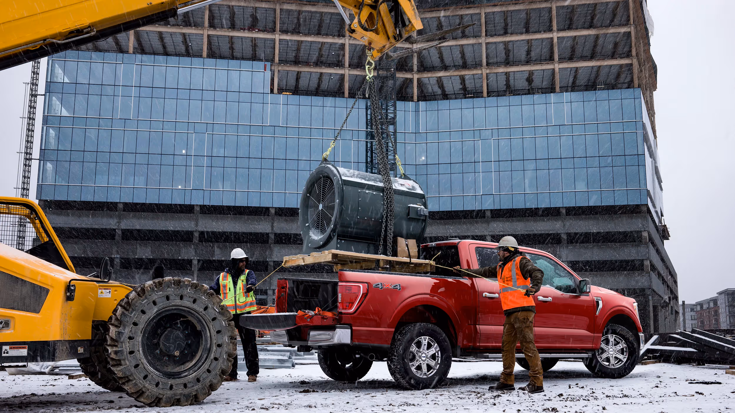 Red Ford F-150 parked at a modern construction site as a crane lowers equipment into place.