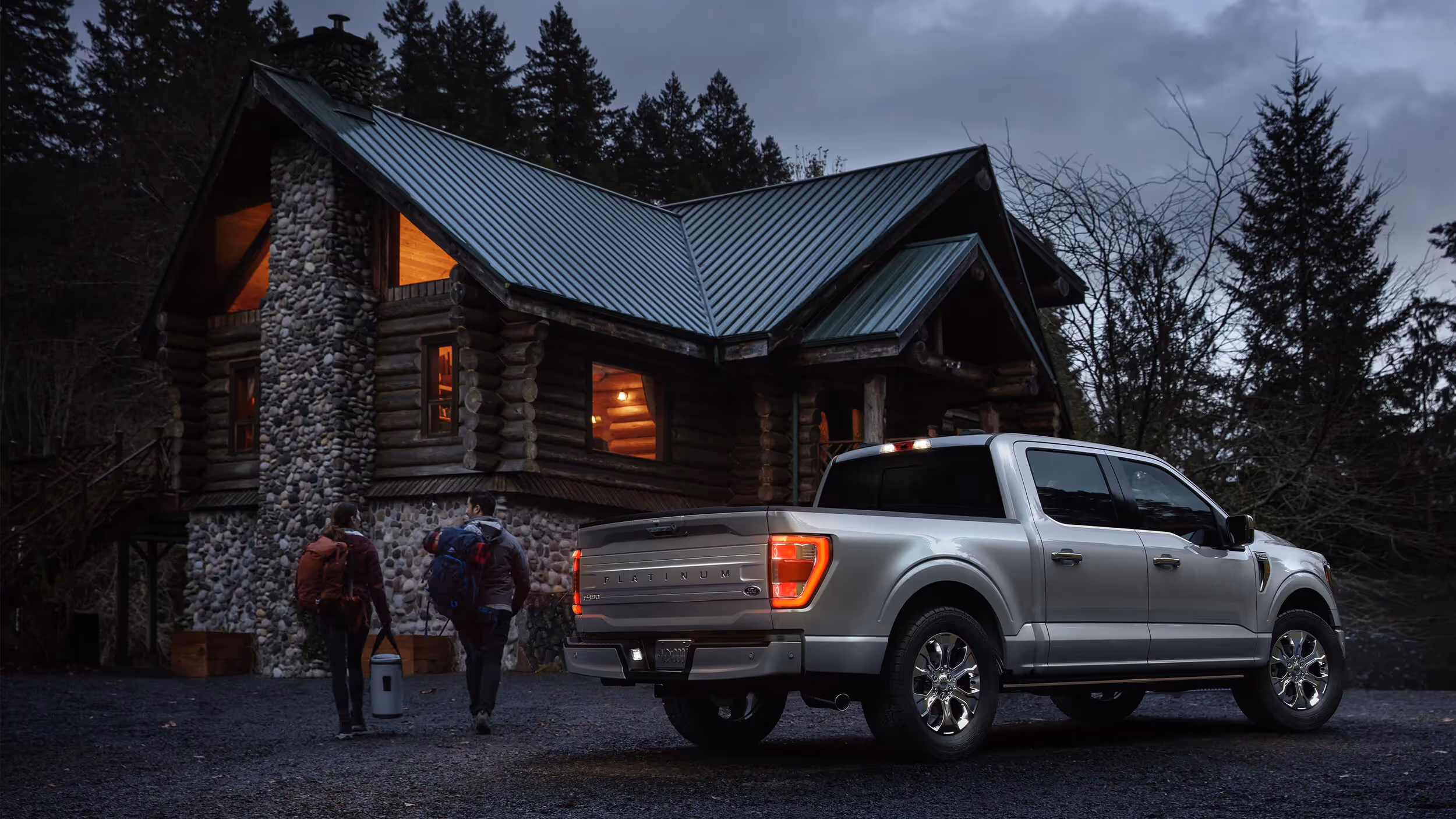 Silver Ford F-150 parked outside a mountain cabin as hikers unload gear at dusk.