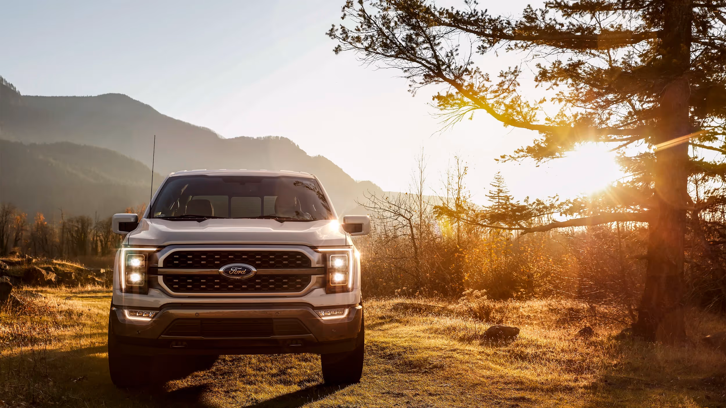 Ford F-150 facing camera at sunrise on an open field surrounded by mountain ridges.