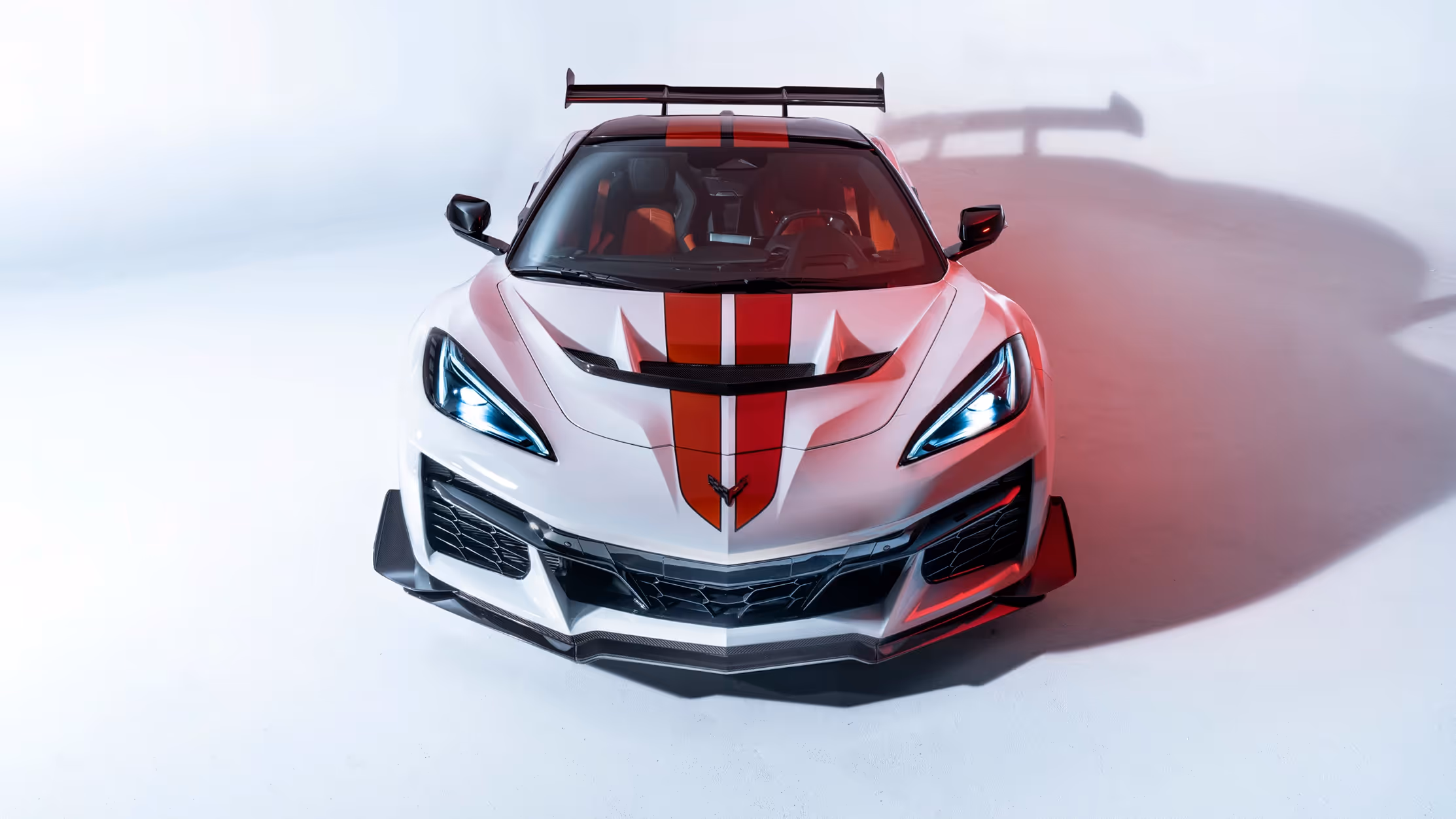 Front-facing studio shot of the Chevrolet Corvette ZR1 with red and black racing stripes under crisp white lighting.