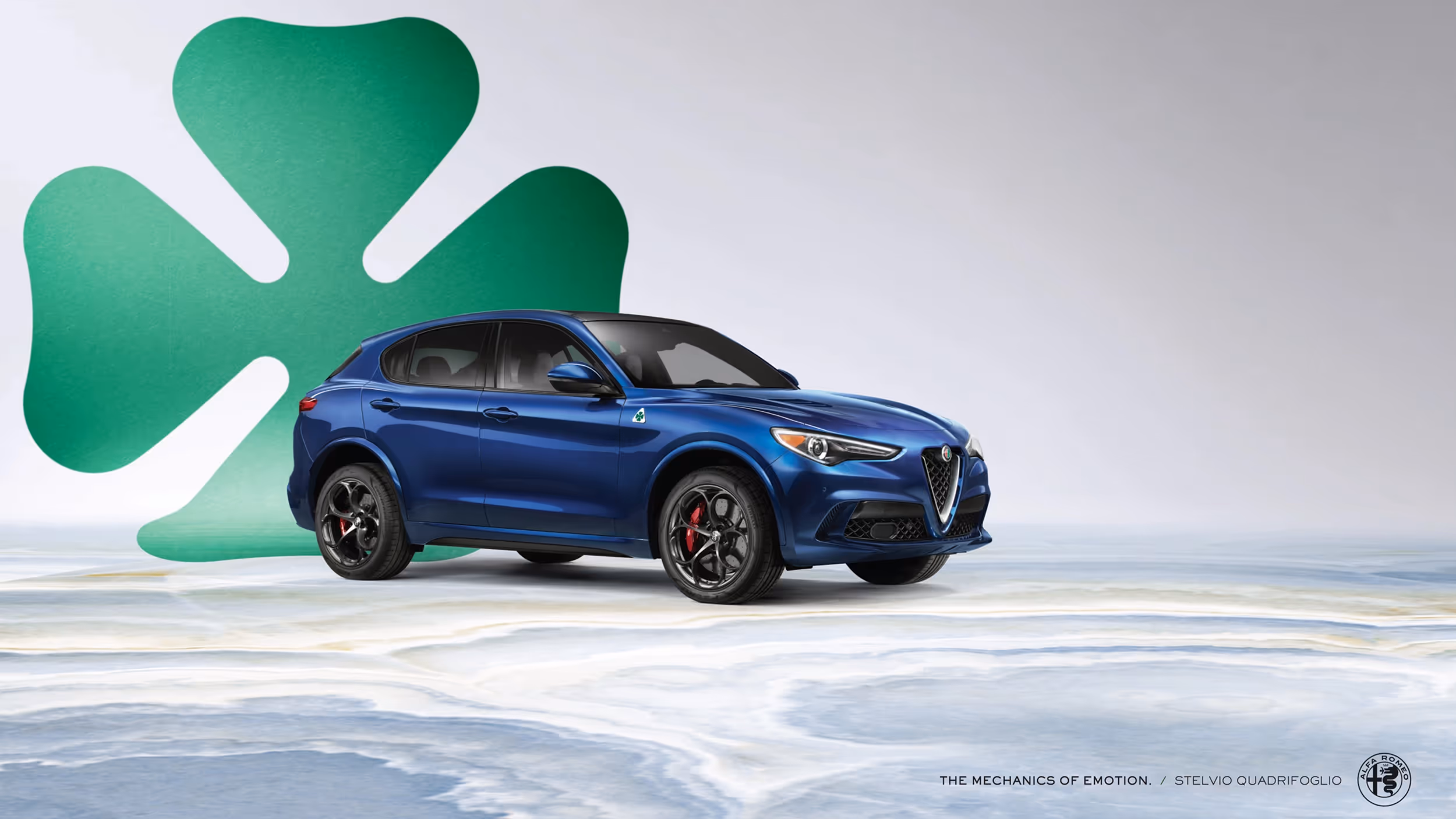 Blue Alfa Romeo Stelvio on a marbled surface with a green cloverleaf background under soft studio lighting.