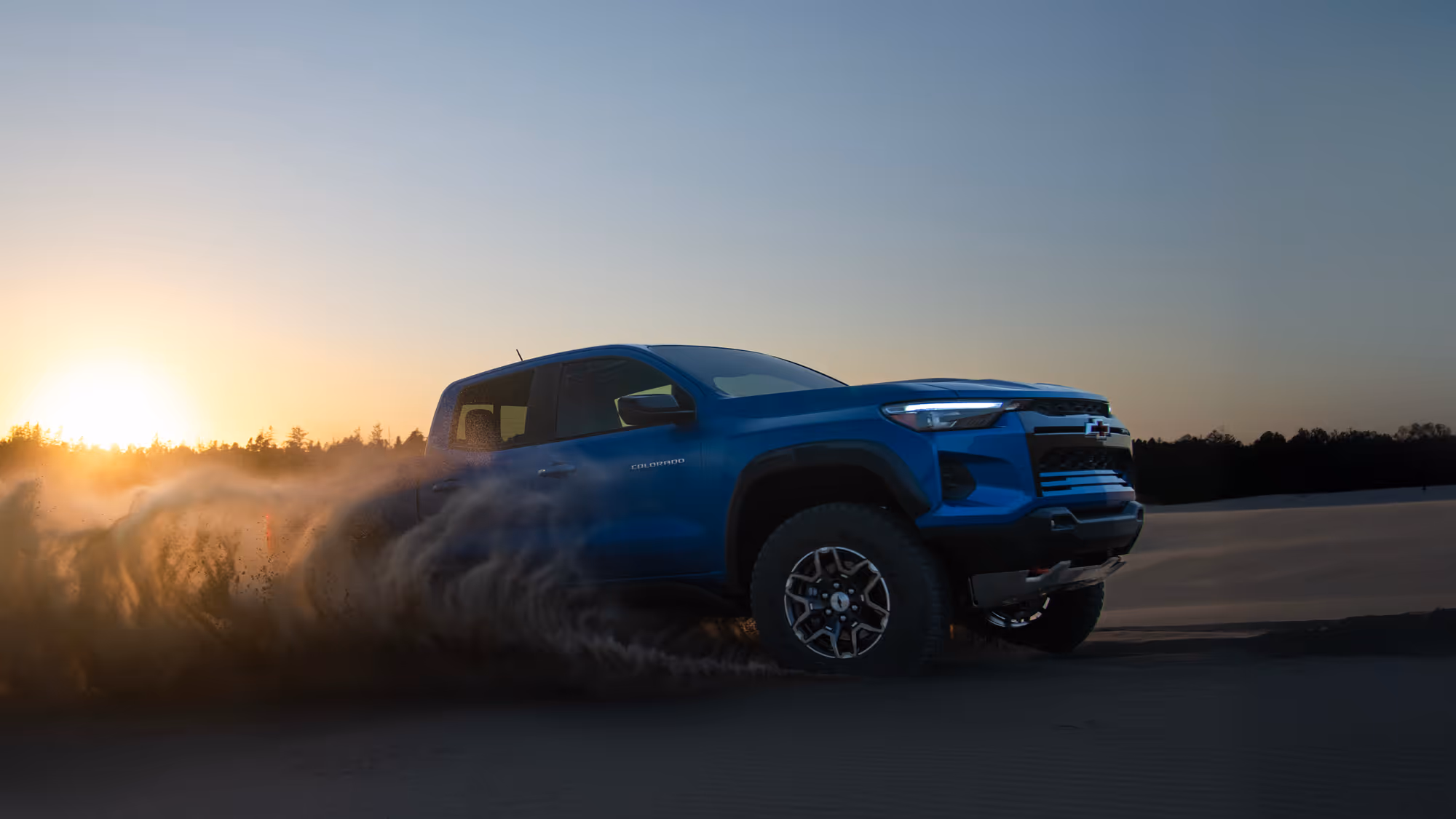 Profile view of Chevy Colorado ZR2 cutting through sand with flying debris in midair.