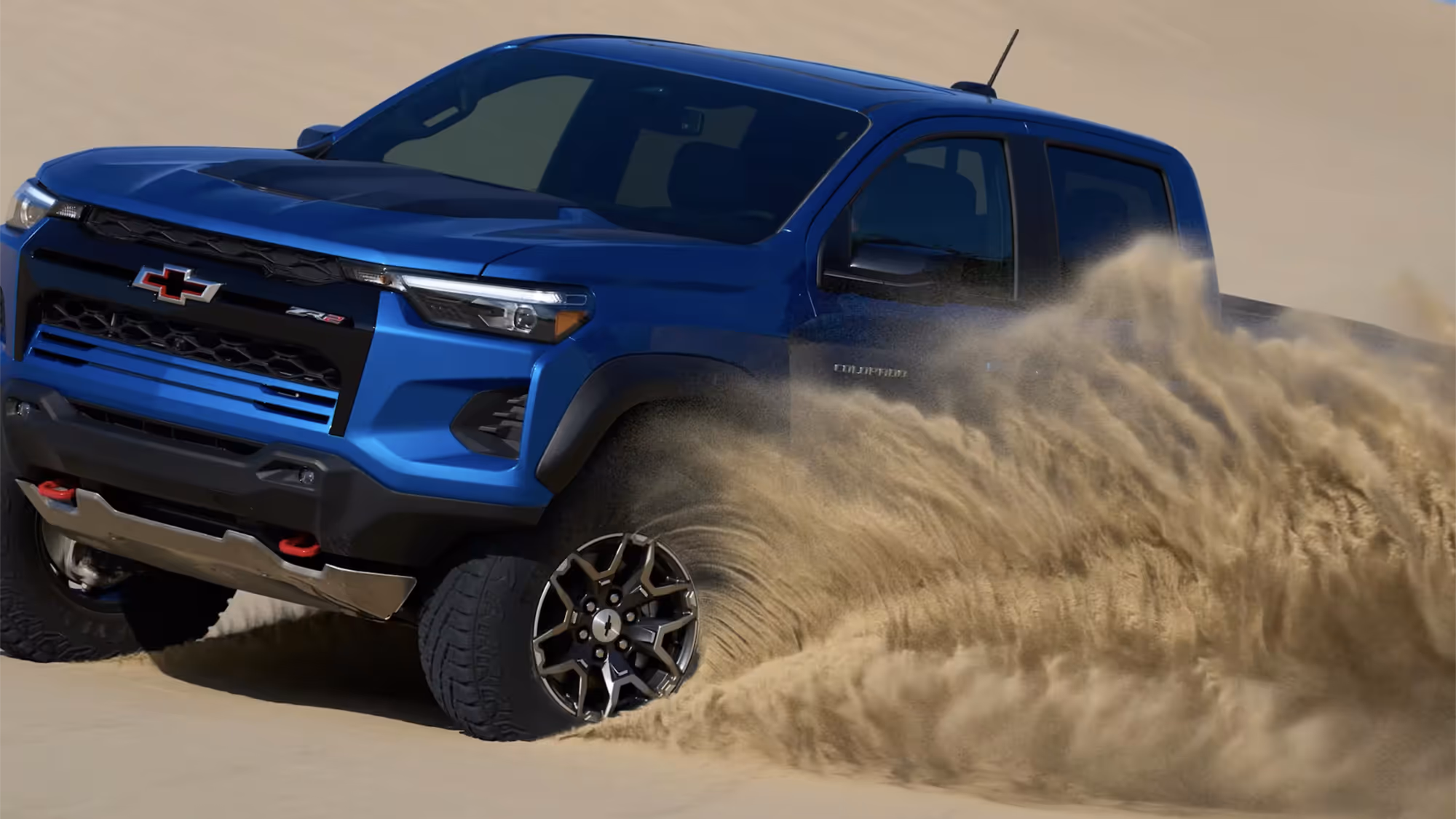 Close-up of Chevy Colorado ZR2 cutting into sand, debris flying from front tires.