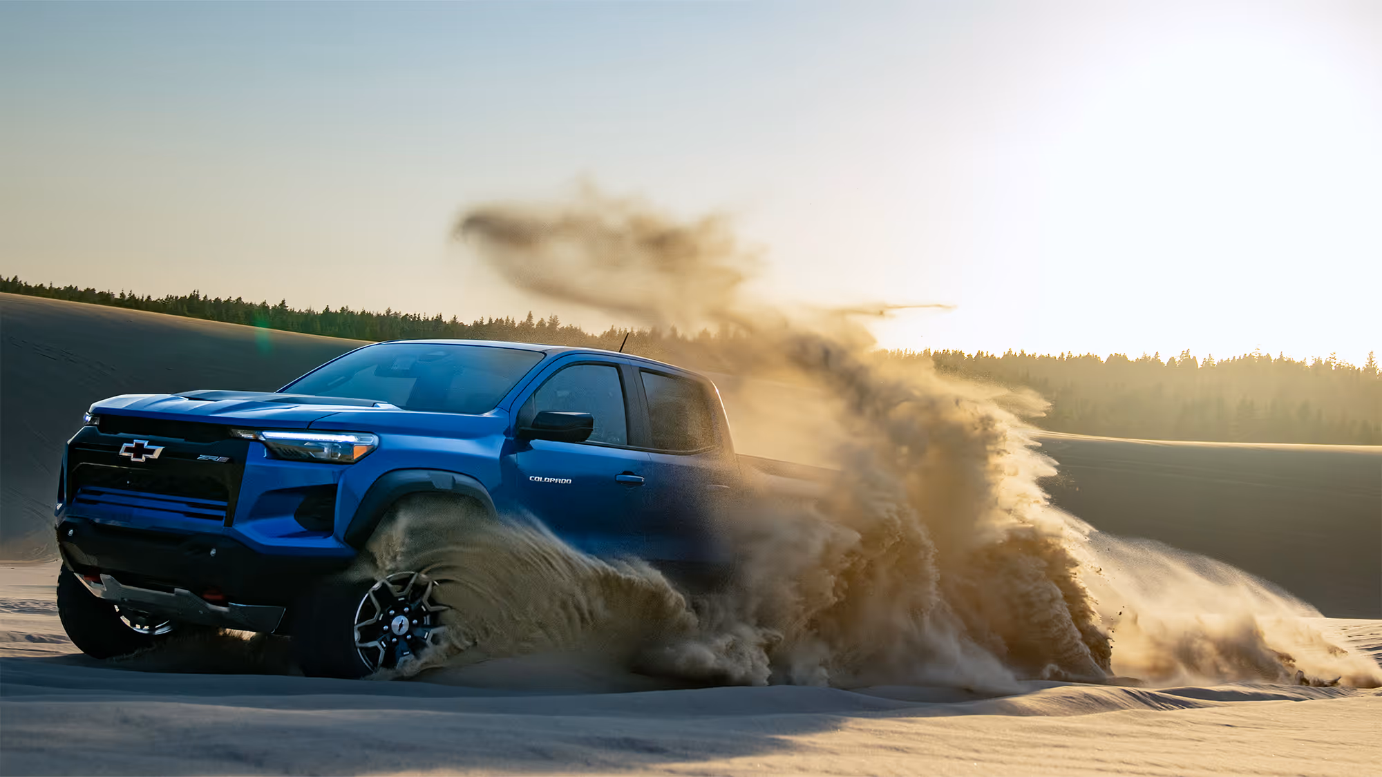 Front three-quarter view of Chevy Colorado ZR2 cutting through sand with flying debris in midair.