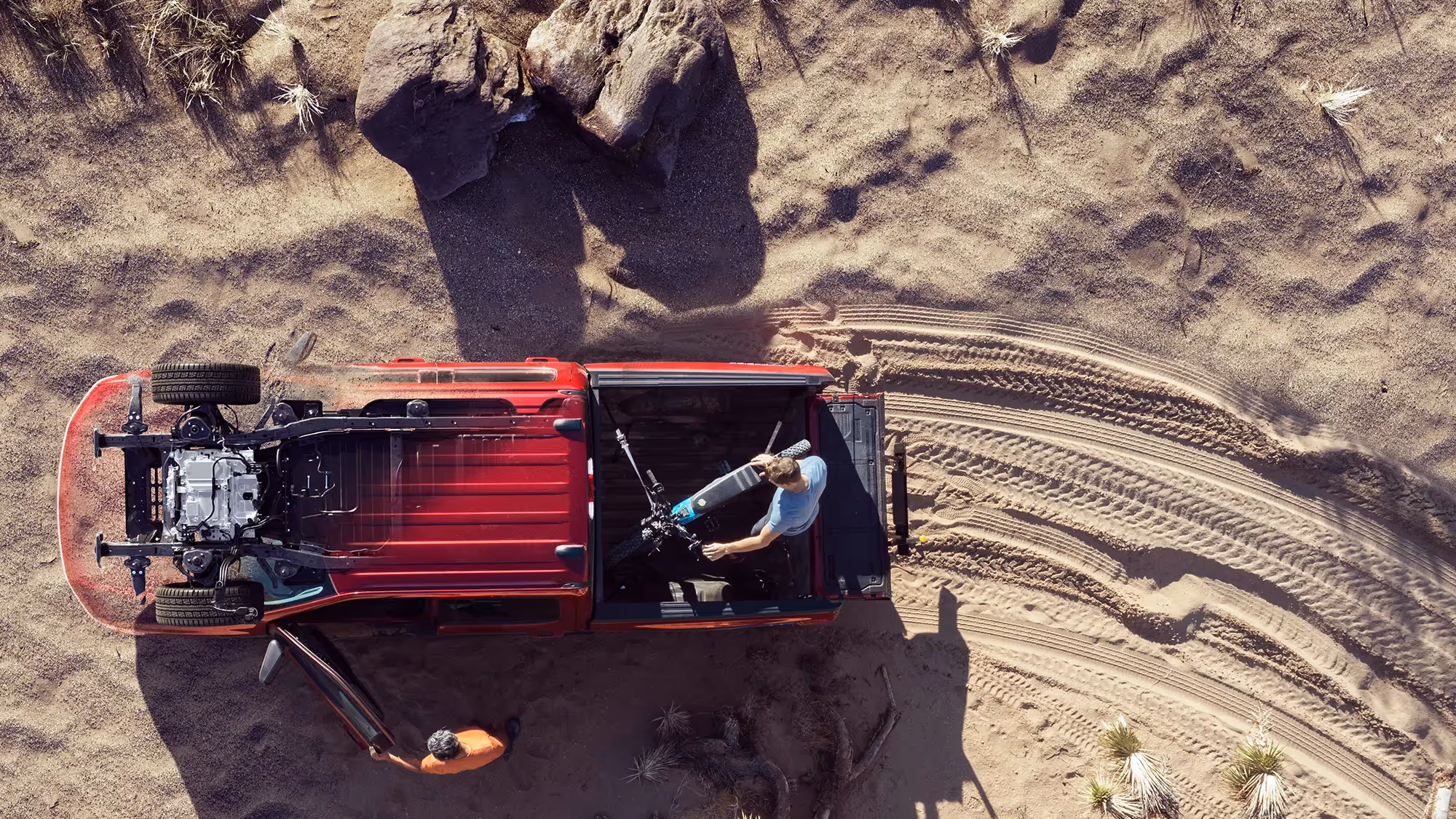 Overhead view of a red Ford F-150 Lightning in the desert, tailgate down with a person setting up equipment on the sand.