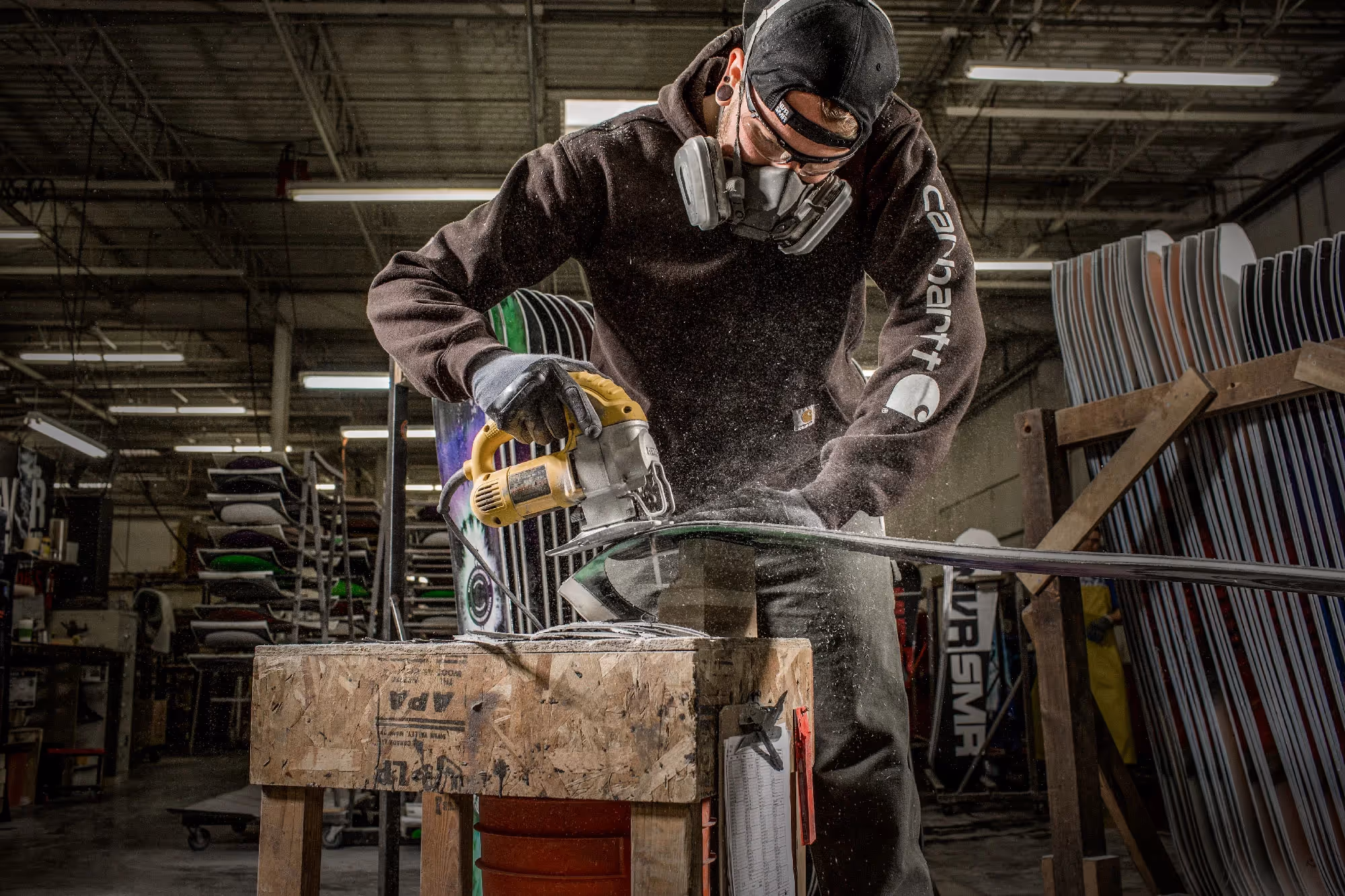 A craftsman wearing a mask and safety glasses cuts metal tubing with a circular saw inside a workshop, sparks flying.