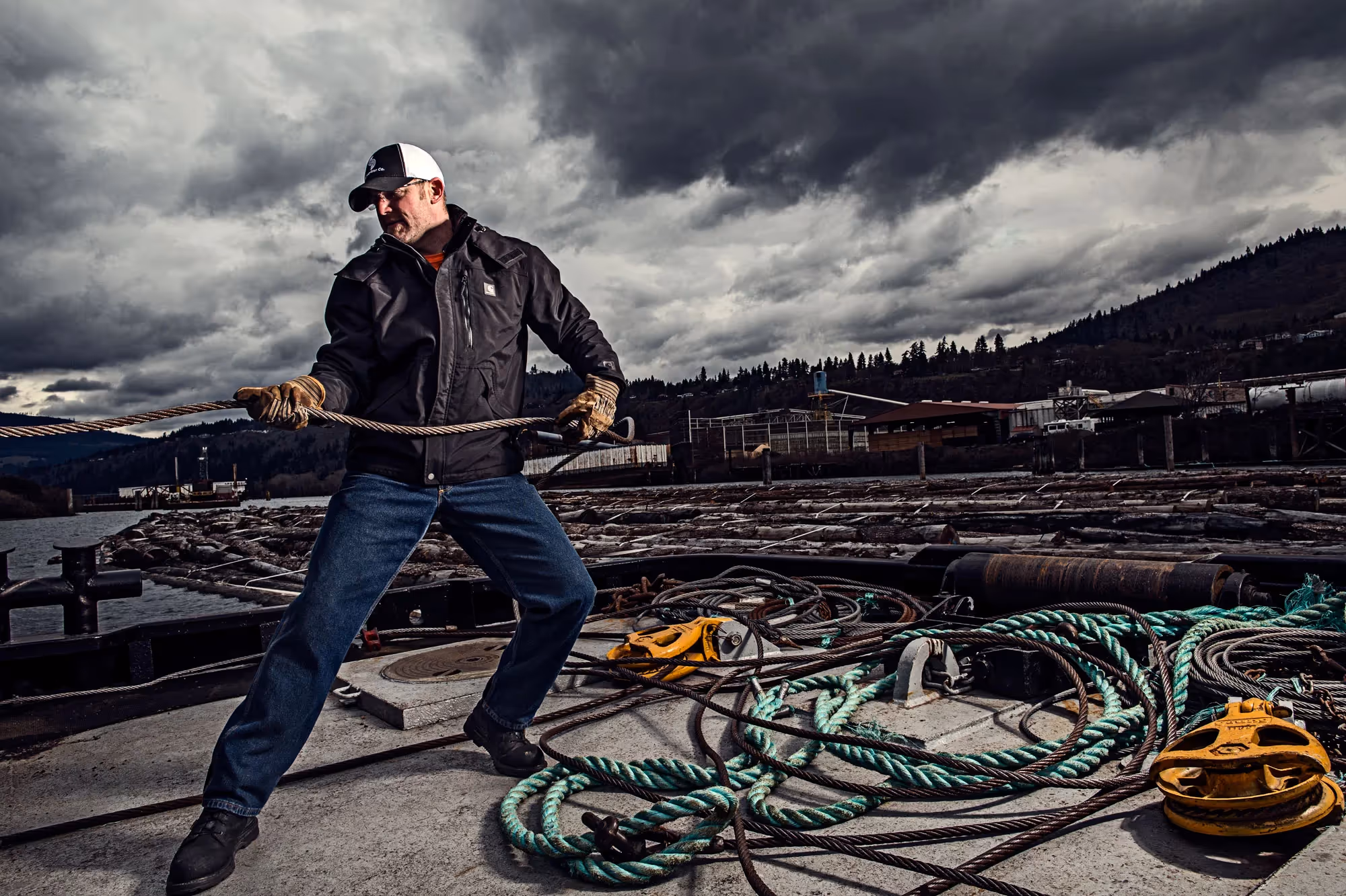 A dockworker pulls thick rope across a wet surface, standing firm against wind and cloud.