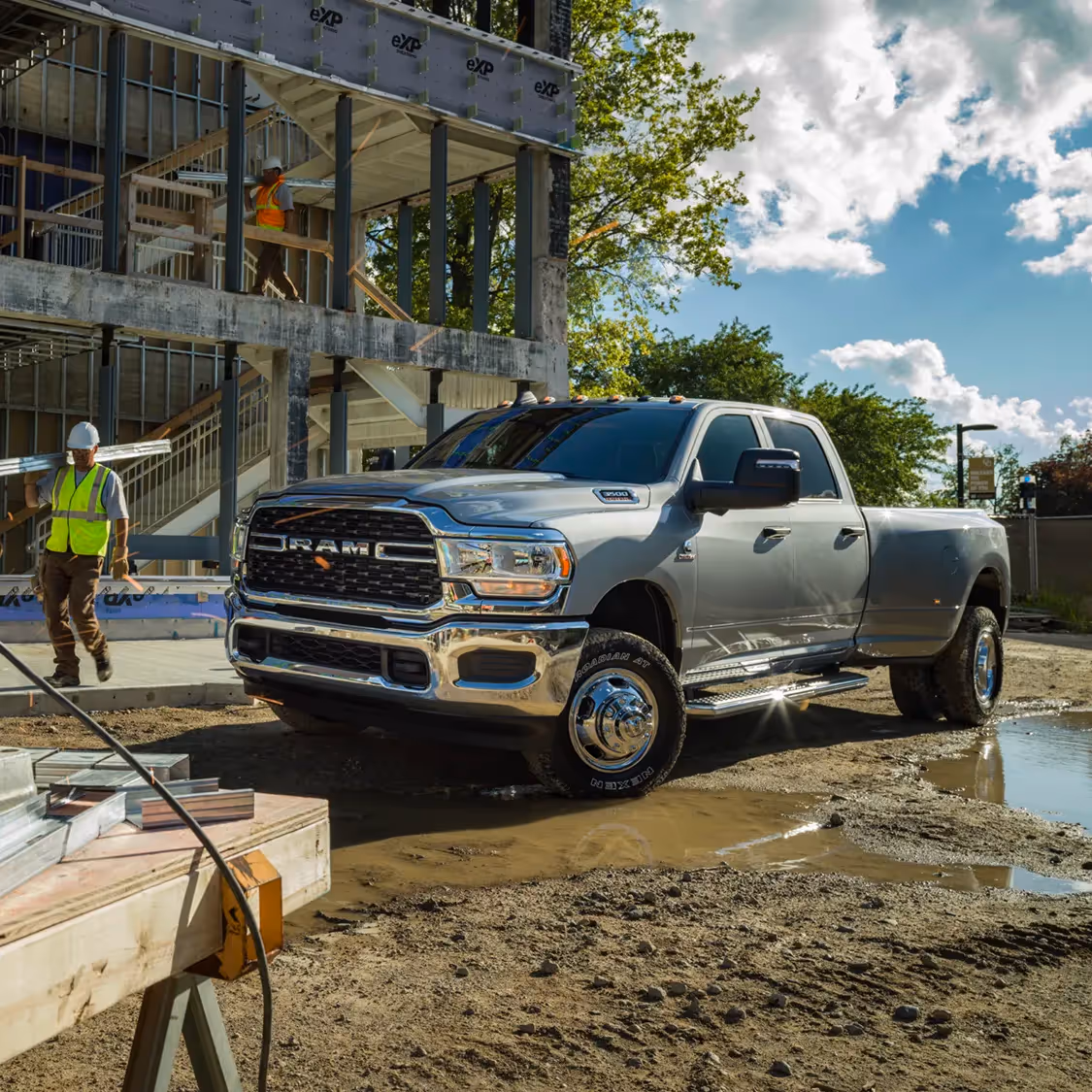 A silver Ram HD pickup parked beside an active construction site with scaffolding and cranes in the background.