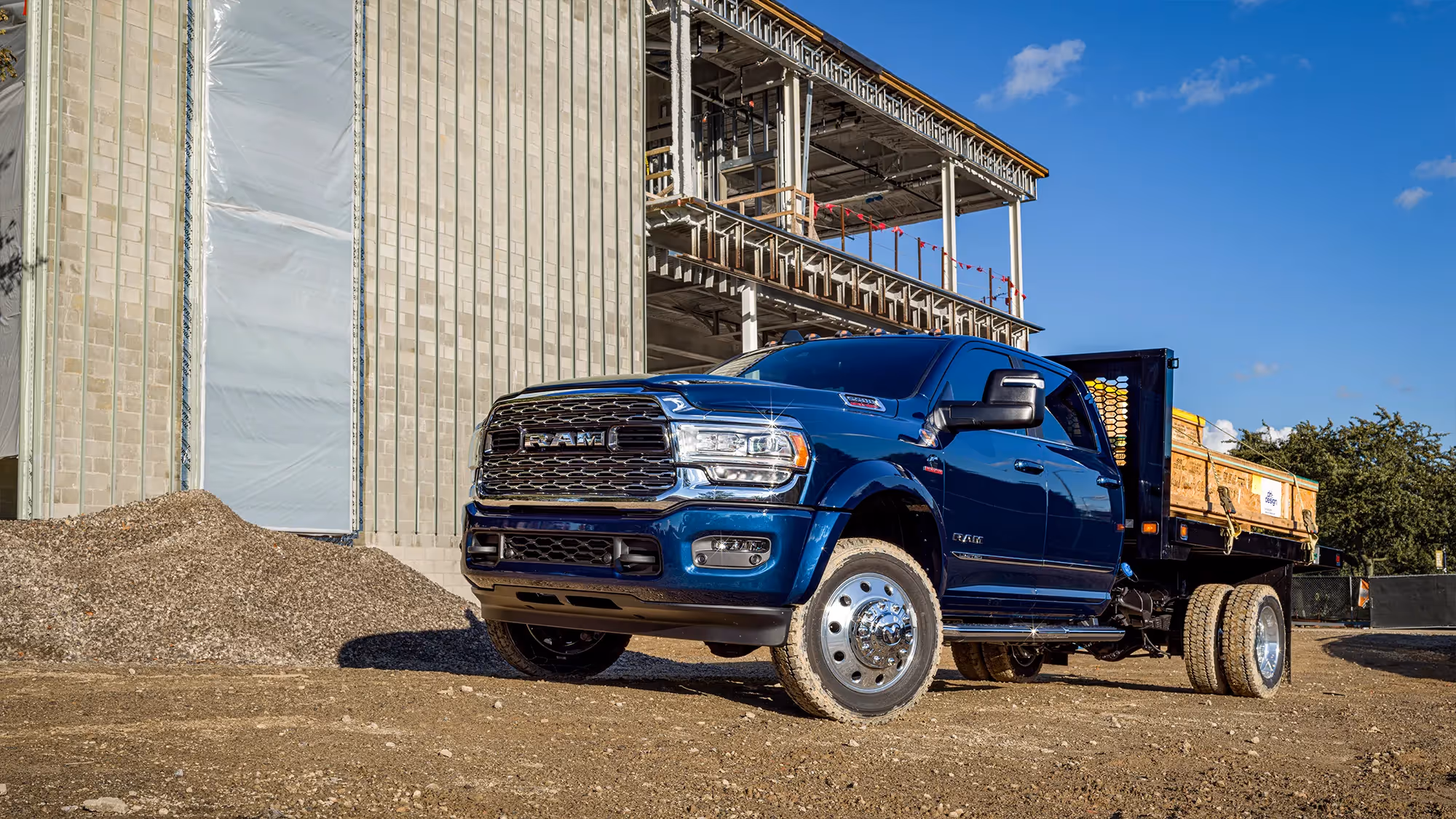 A blue Ram HD truck hauls material on a dirt lot surrounded by unfinished concrete structures.