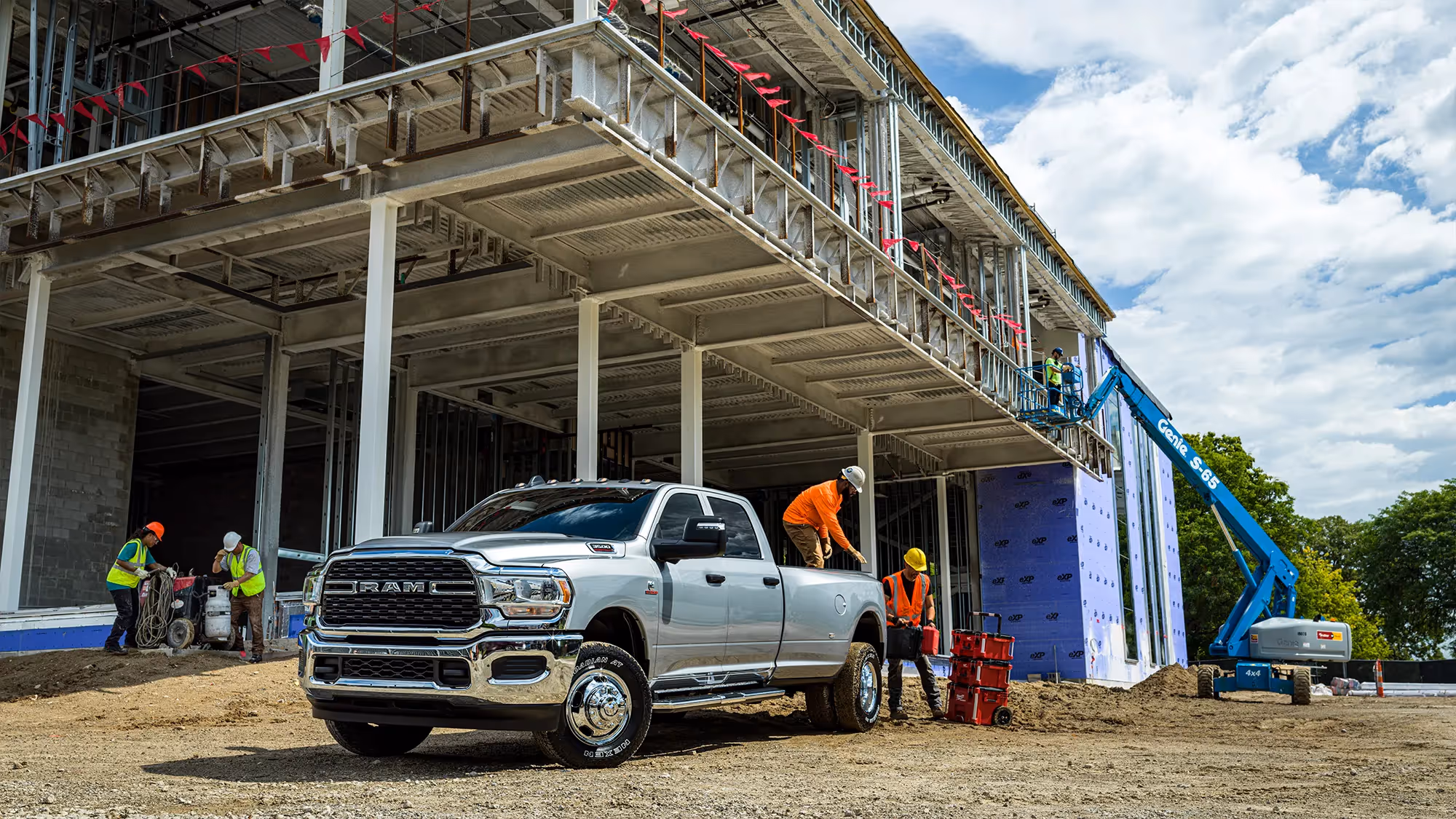 A silver Ram HD parked under a building frame as workers install insulation on the upper levels.