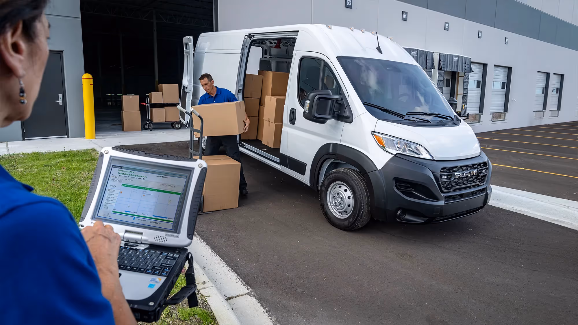 A logistics worker enters data on a tablet while boxes are loaded into a white Ram ProMaster van.
