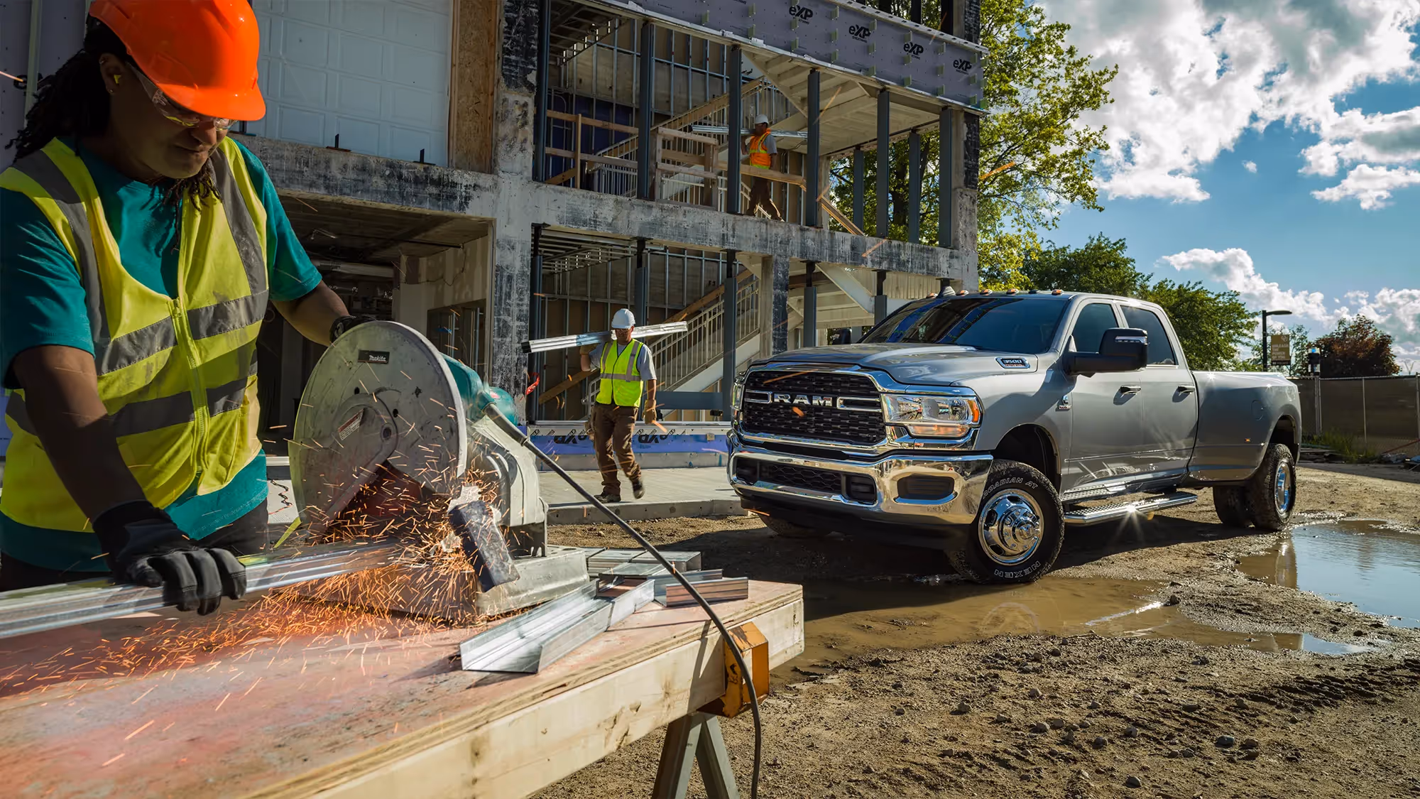 A silver Ram HD pickup parked beside an active construction site with scaffolding and cranes in the background.