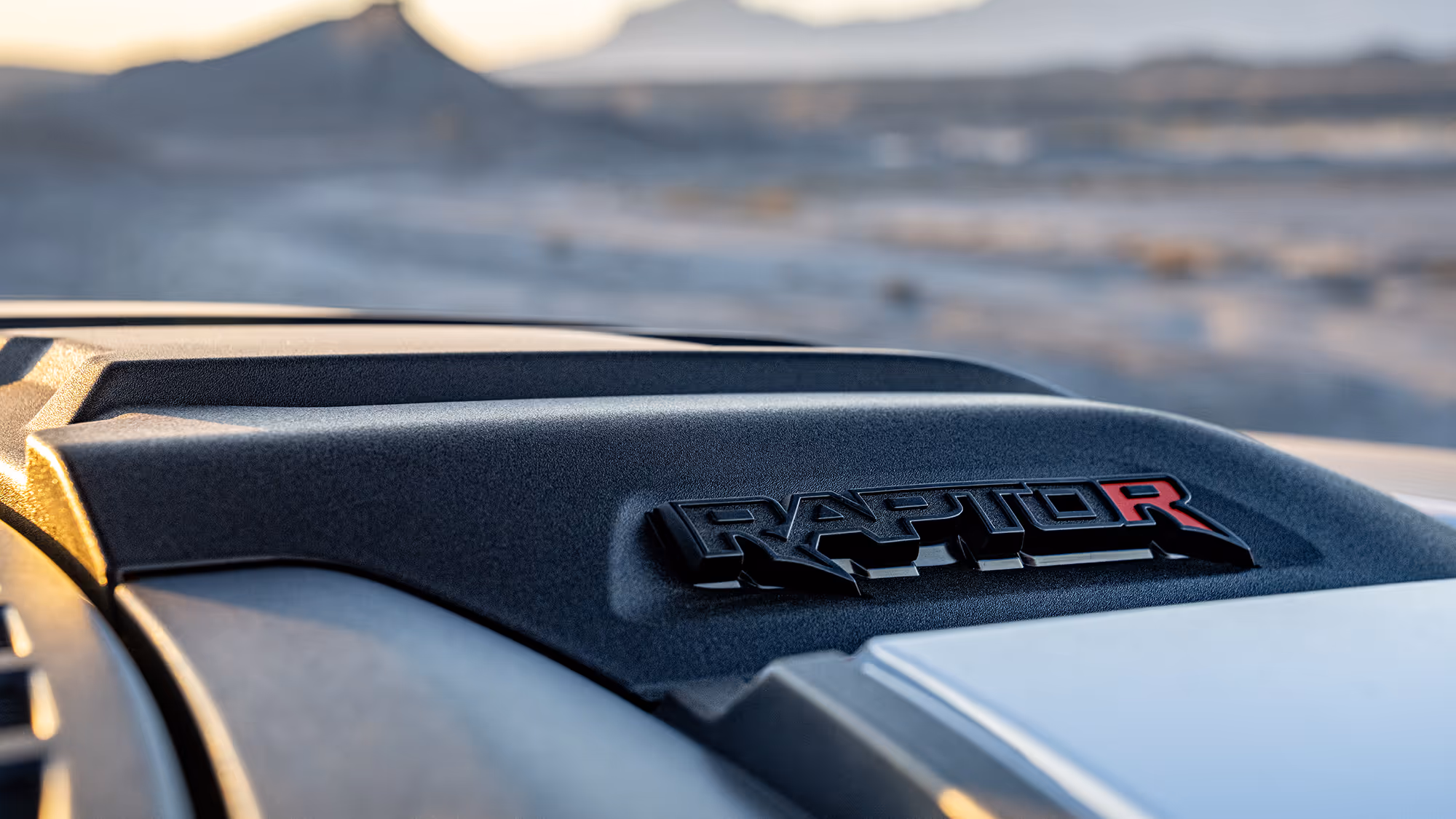 Close-up of Ford Raptor R hood badge with blurred desert landscape in background