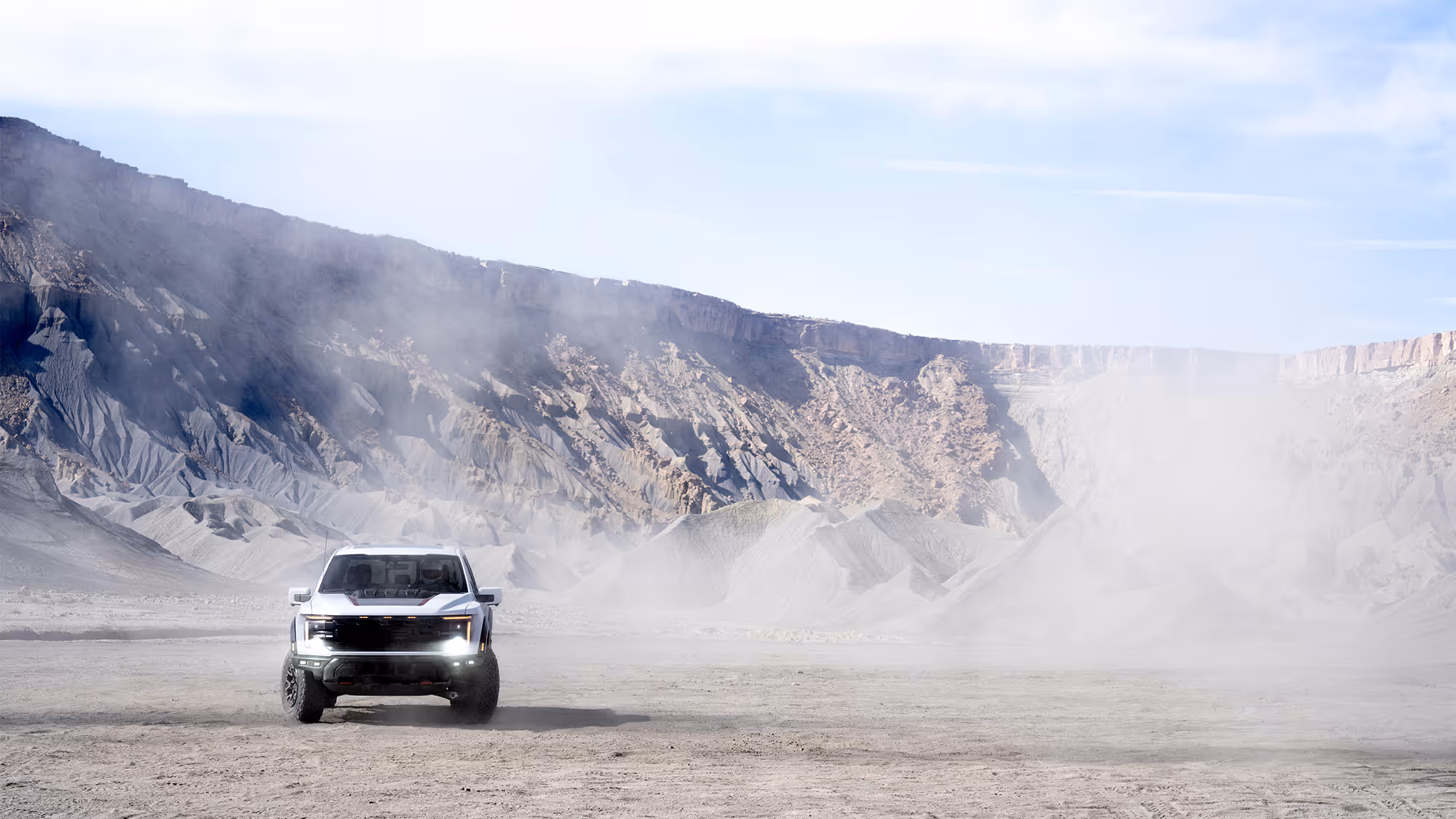 Ford Raptor R driving through wide desert basin with dust trail and cliffs in background