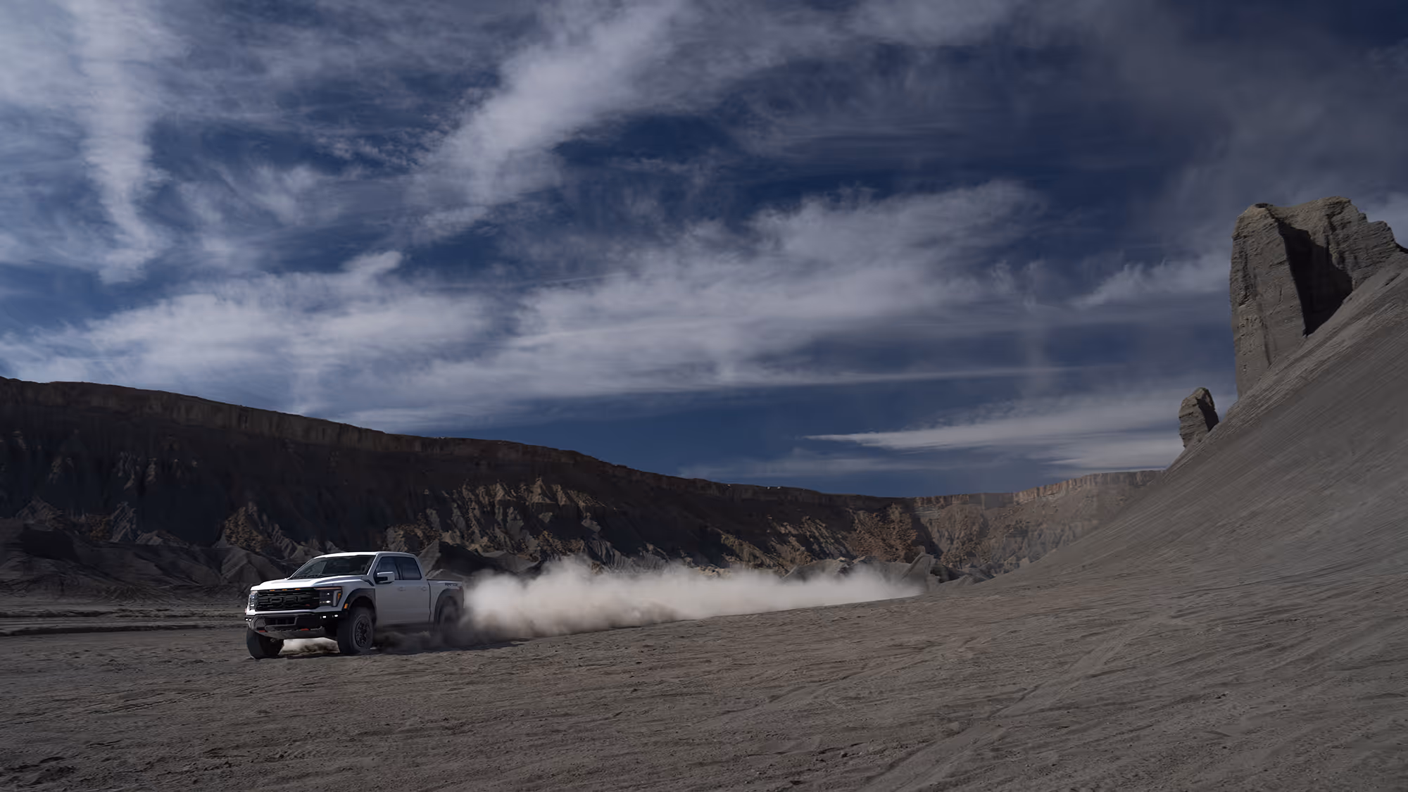 Ford Raptor R speeding through wide desert valley leaving long dust trail under dramatic sky