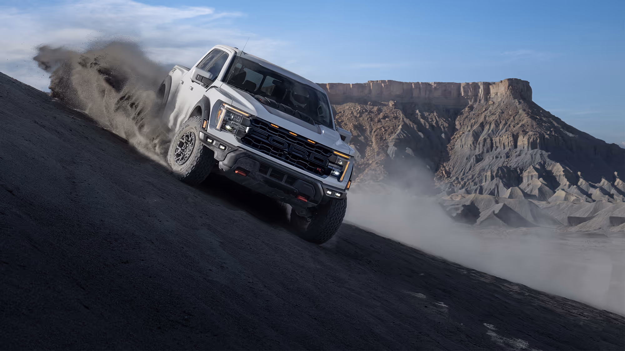 Ford Raptor R driving diagonally down rugged hillside with dust and canyon backdrop
