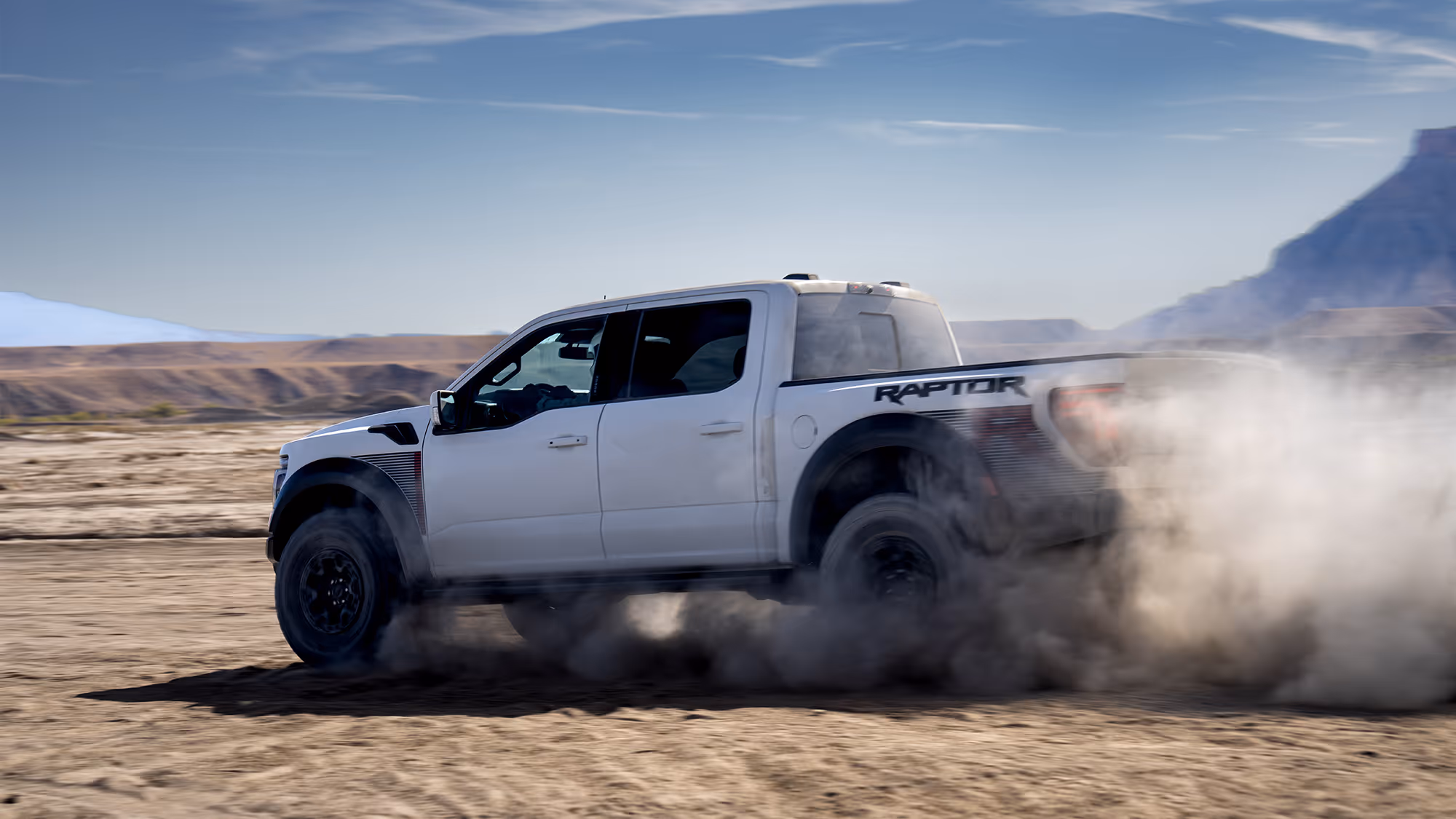 Ford Raptor R driving across desert terrain kicking up dust with mountains in background
