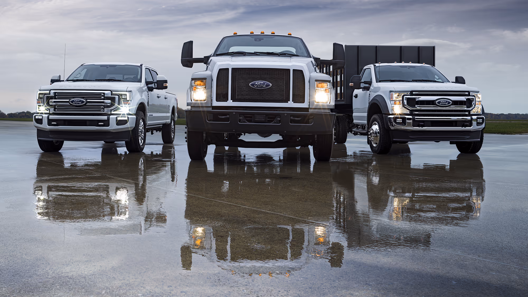 Ford Super Duty trucks lined up on wet tarmac with reflections and headlights on